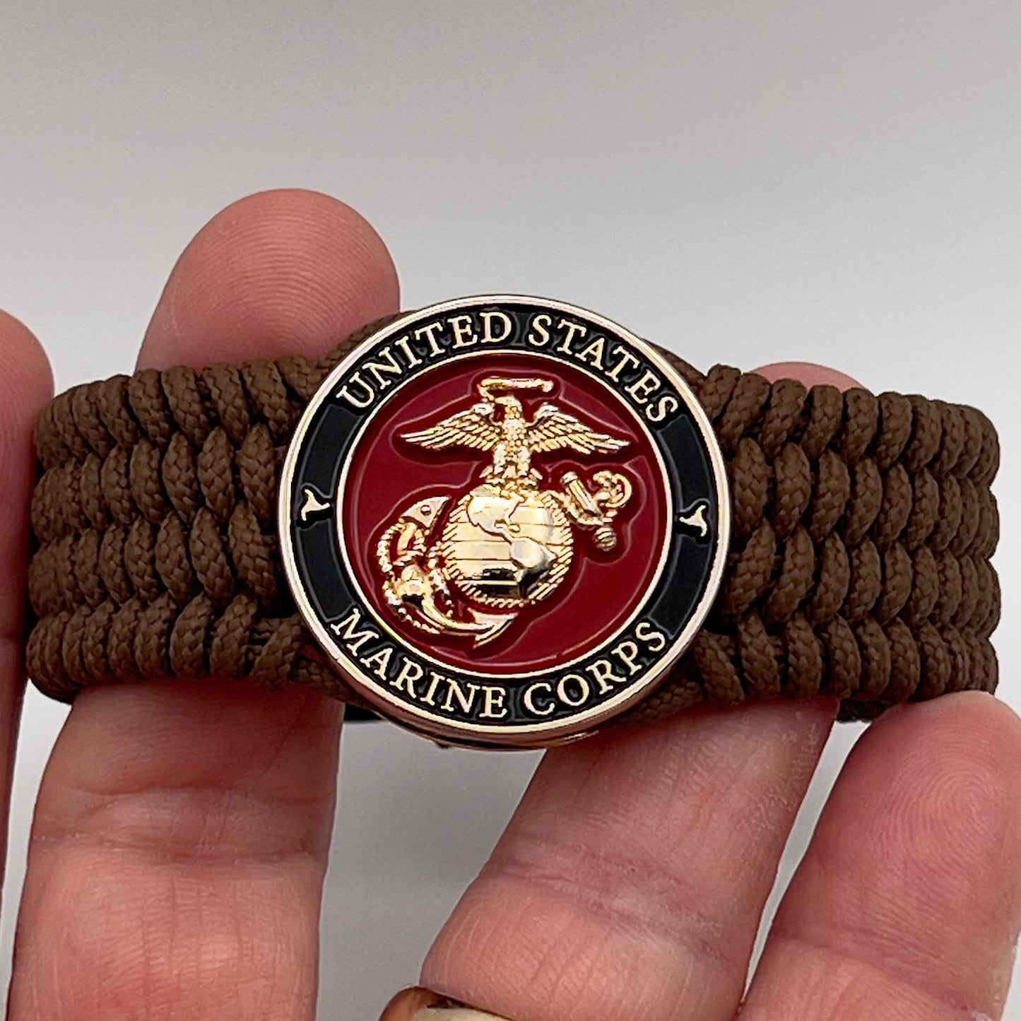 Thin, medium width, flexible and comfortable braided United States Marine Corps bracelet featuring a 24K gold plated USMC officer Eagle Globe and Anchor medallion, a gold Cobra style tactical buckle and woven with Coyote Brown Type-1 paracord.