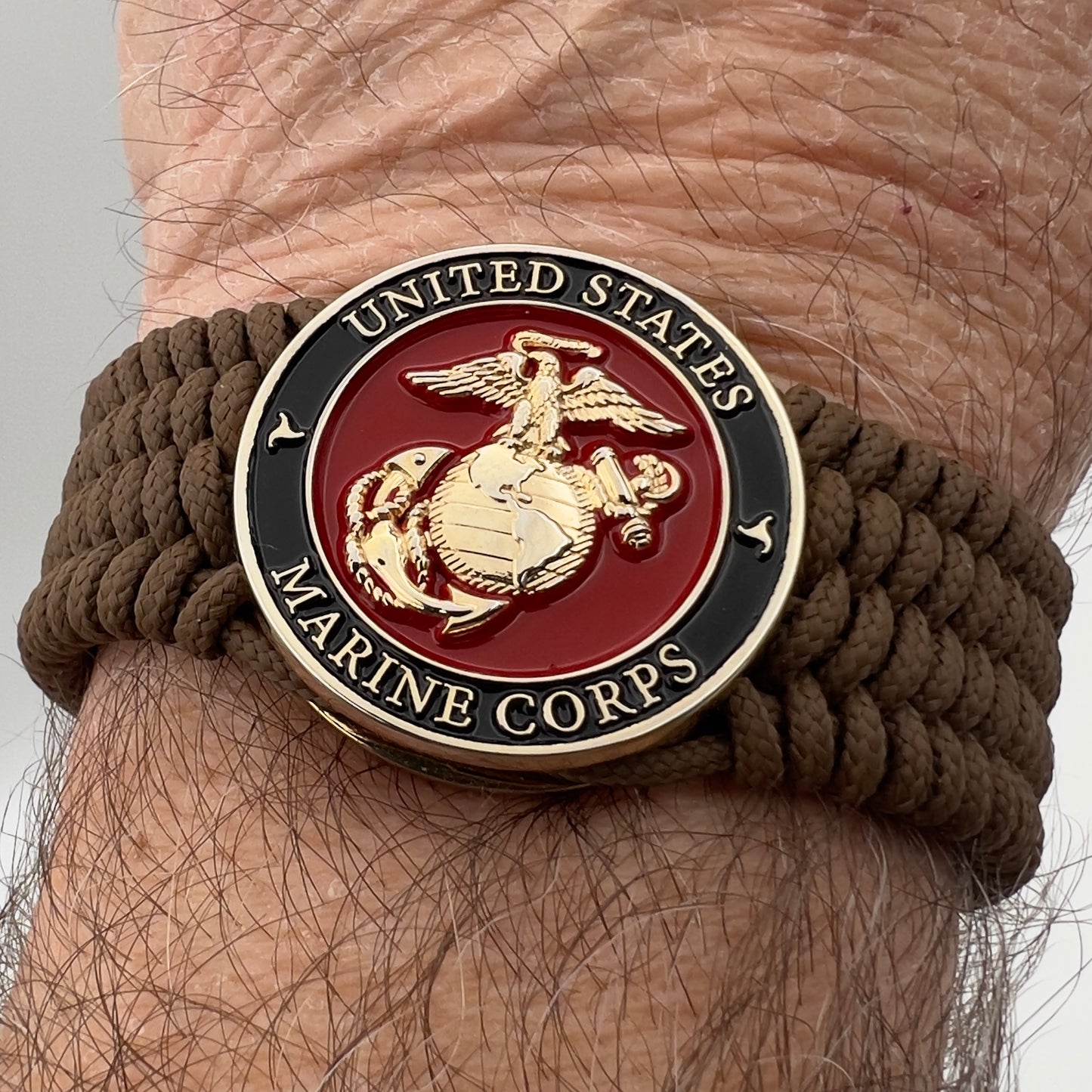Thin, medium width, flexible and comfortable braided United States Marine Corps bracelet featuring a 24K gold plated USMC officer Eagle Globe and Anchor medallion, a gold Cobra style tactical buckle and woven with Coyote Brown Type-1 paracord.