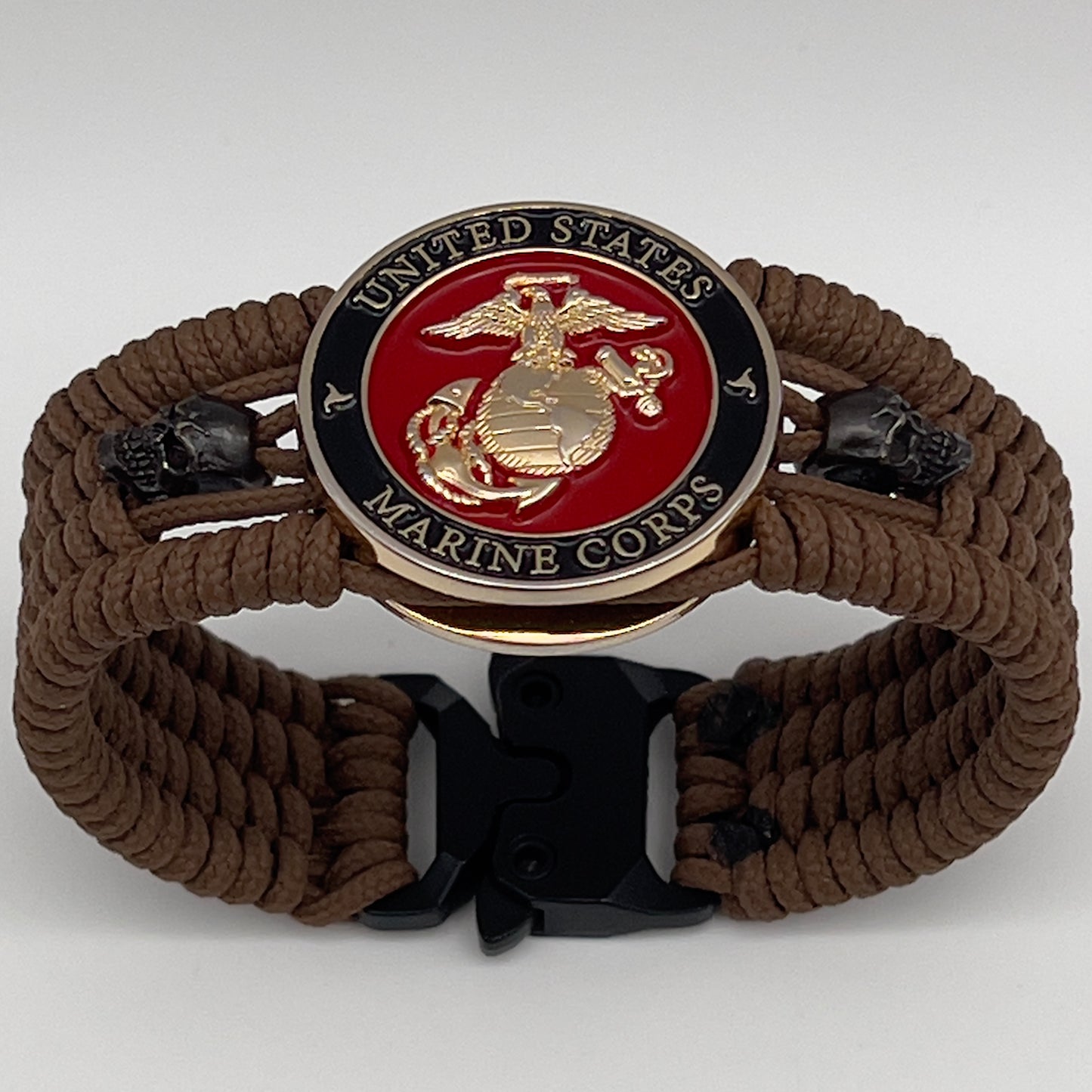 Thin, medium width, flexible and comfortable braided United States Marine Corps bracelet featuring a 24K gold plated USMC officer Eagle Globe and Anchor medallion, two black micro skulls, a black Cobra style tactical buckle and woven with Coyote Brown Type-1 paracord.