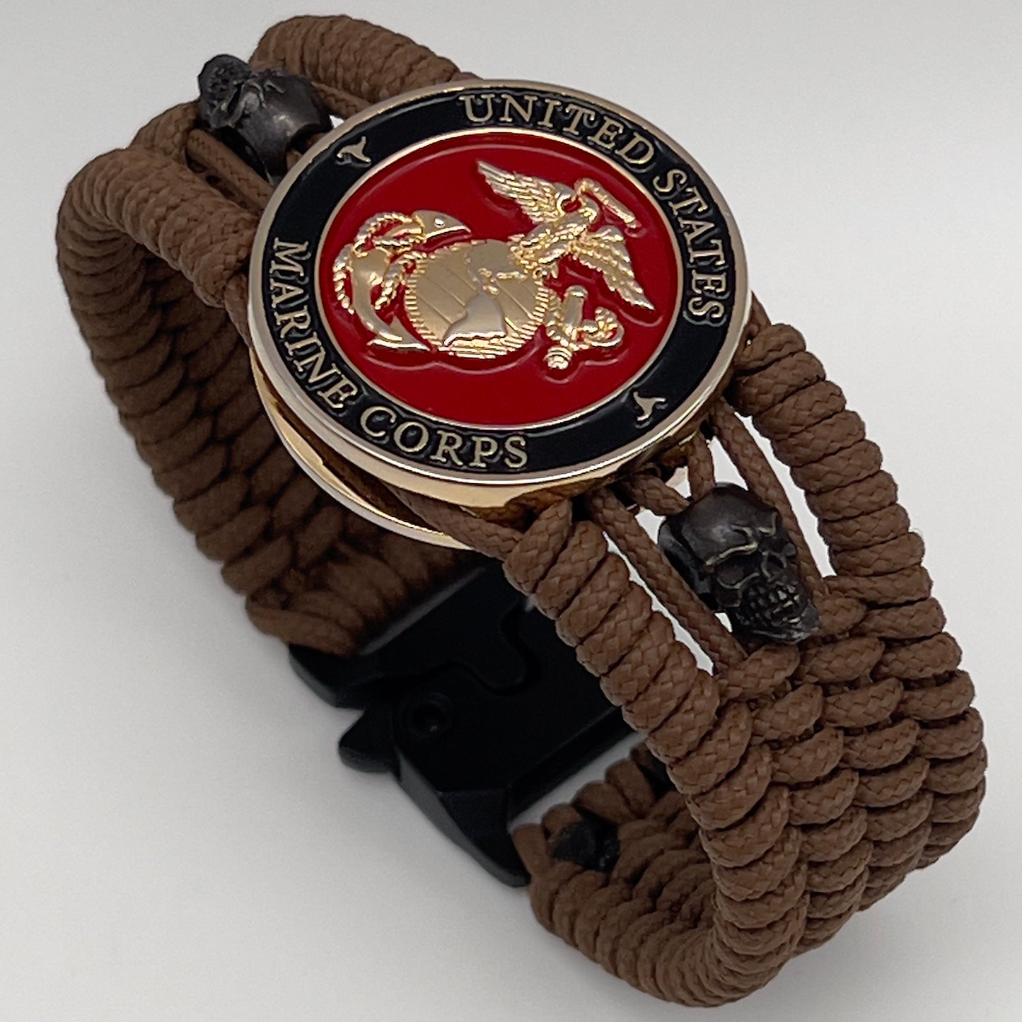 Thin, medium width, flexible and comfortable braided United States Marine Corps bracelet featuring a 24K gold plated USMC officer Eagle Globe and Anchor medallion, two black micro skulls, a black Cobra style tactical buckle and woven with Coyote Brown Type-1 paracord.