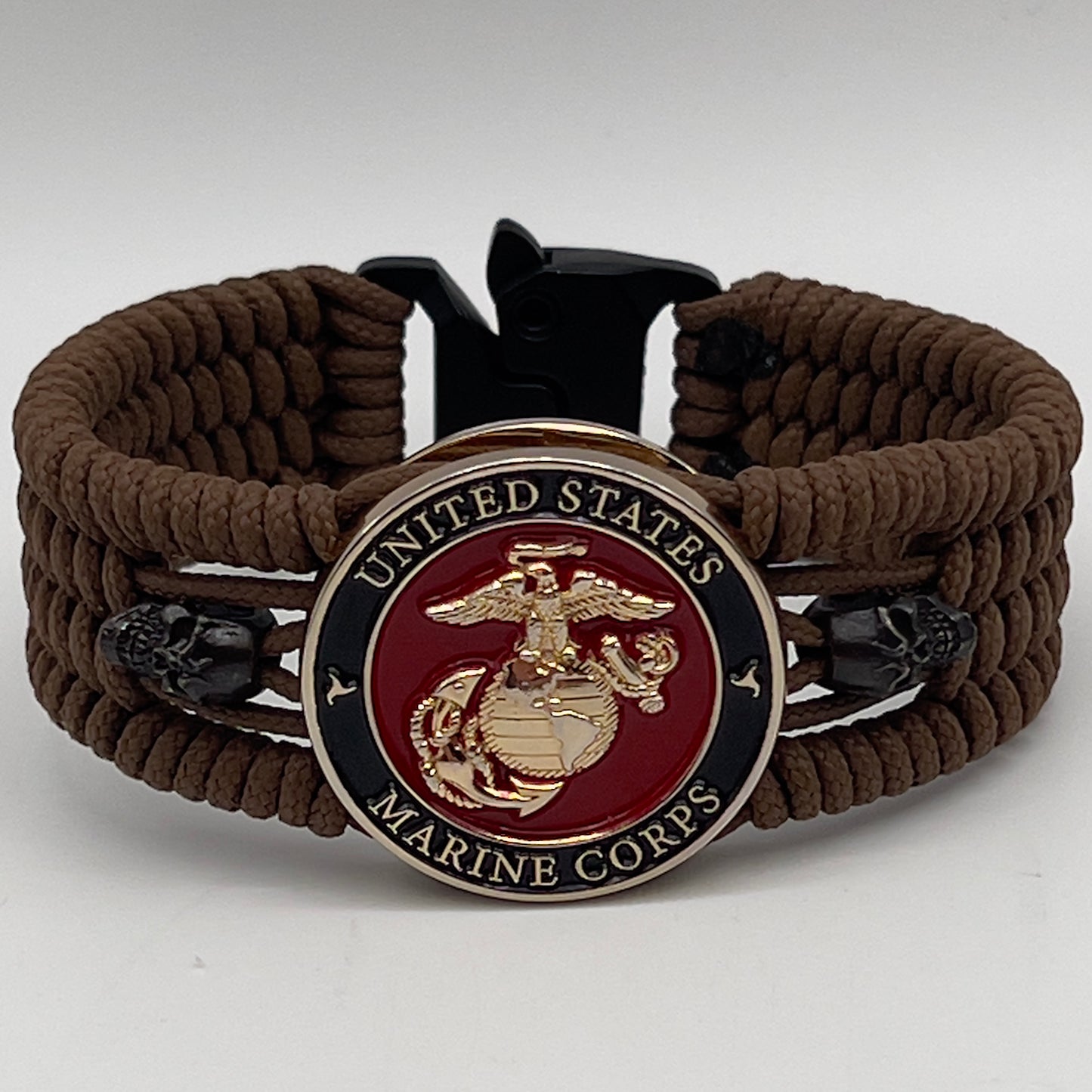 Thin, medium width, flexible and comfortable braided United States Marine Corps bracelet featuring a 24K gold plated USMC officer Eagle Globe and Anchor medallion, two black micro skulls, a black Cobra style tactical buckle and woven with Coyote Brown Type-1 paracord.