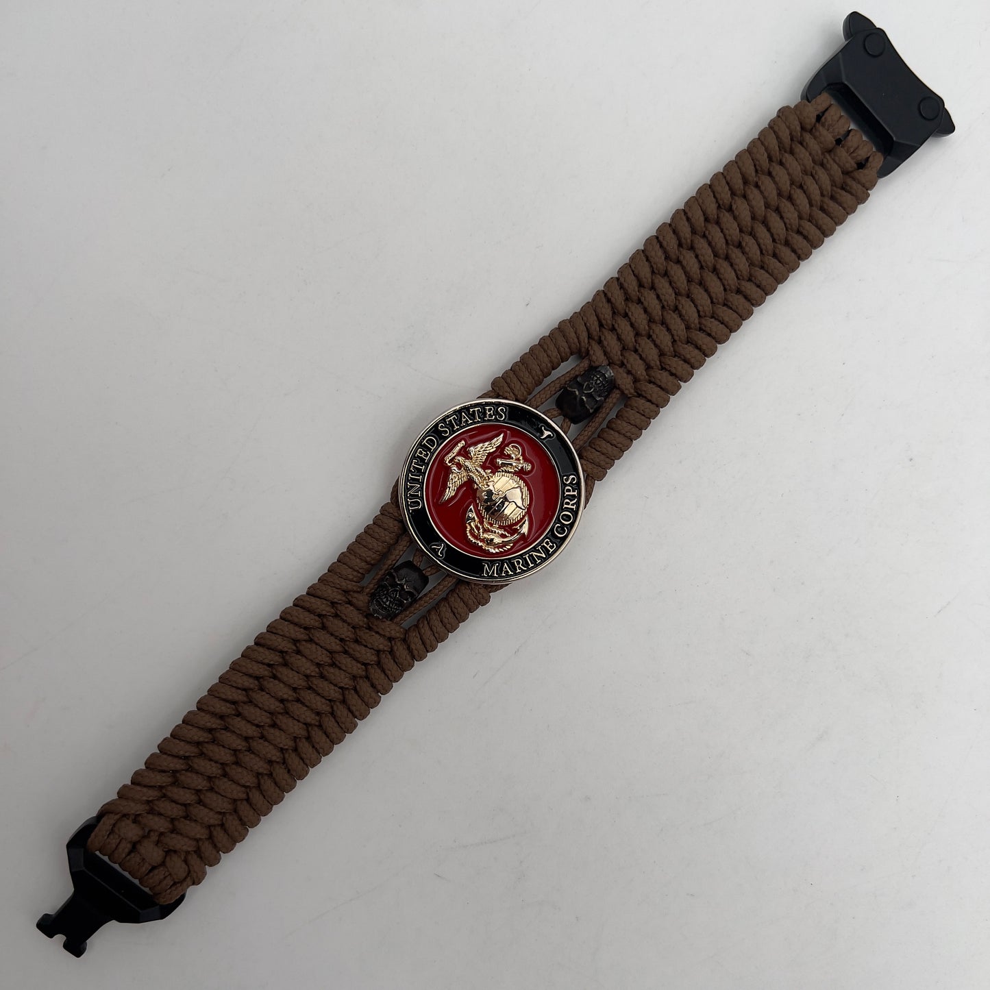 Thin, medium width, flexible and comfortable braided United States Marine Corps bracelet featuring a 24K gold plated USMC officer Eagle Globe and Anchor medallion, two black micro skulls, a black Cobra style tactical buckle and woven with Coyote Brown Type-1 paracord.