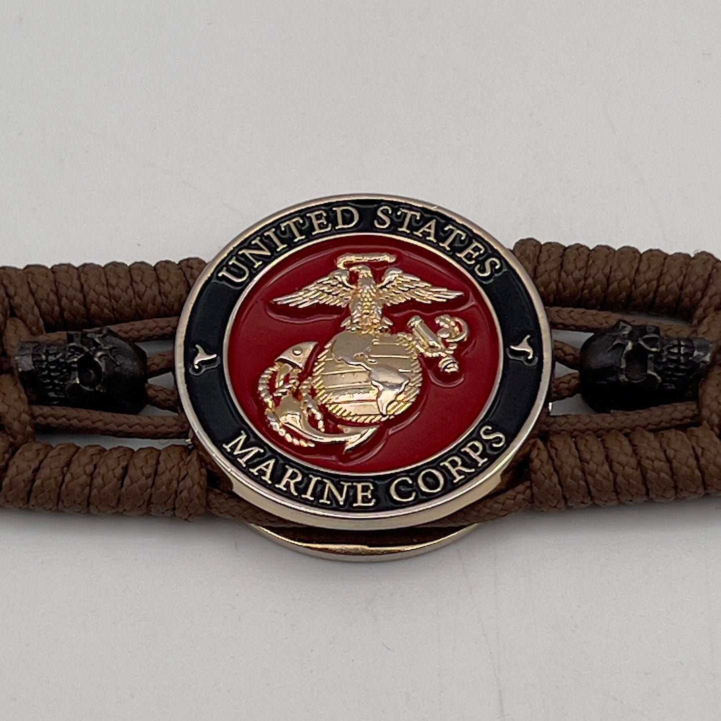 Thin, medium width, flexible and comfortable braided United States Marine Corps bracelet featuring a 24K gold plated USMC officer Eagle Globe and Anchor medallion, two black micro skulls, a black Cobra style tactical buckle and woven with Coyote Brown Type-1 paracord.