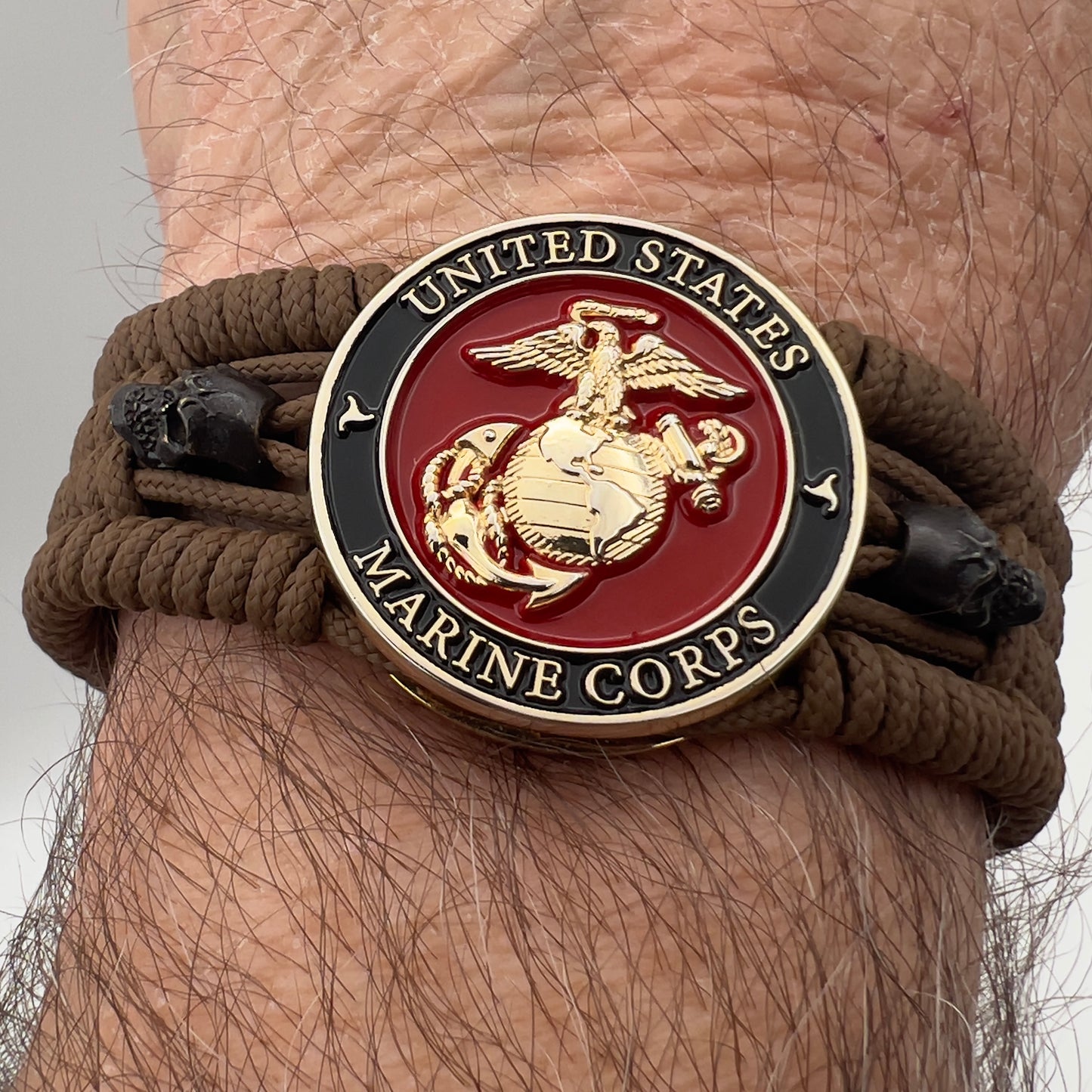 Thin, medium width, flexible and comfortable braided United States Marine Corps bracelet featuring a 24K gold plated USMC officer Eagle Globe and Anchor medallion, two black micro skulls, a black Cobra style tactical buckle and woven with Coyote Brown Type-1 paracord.