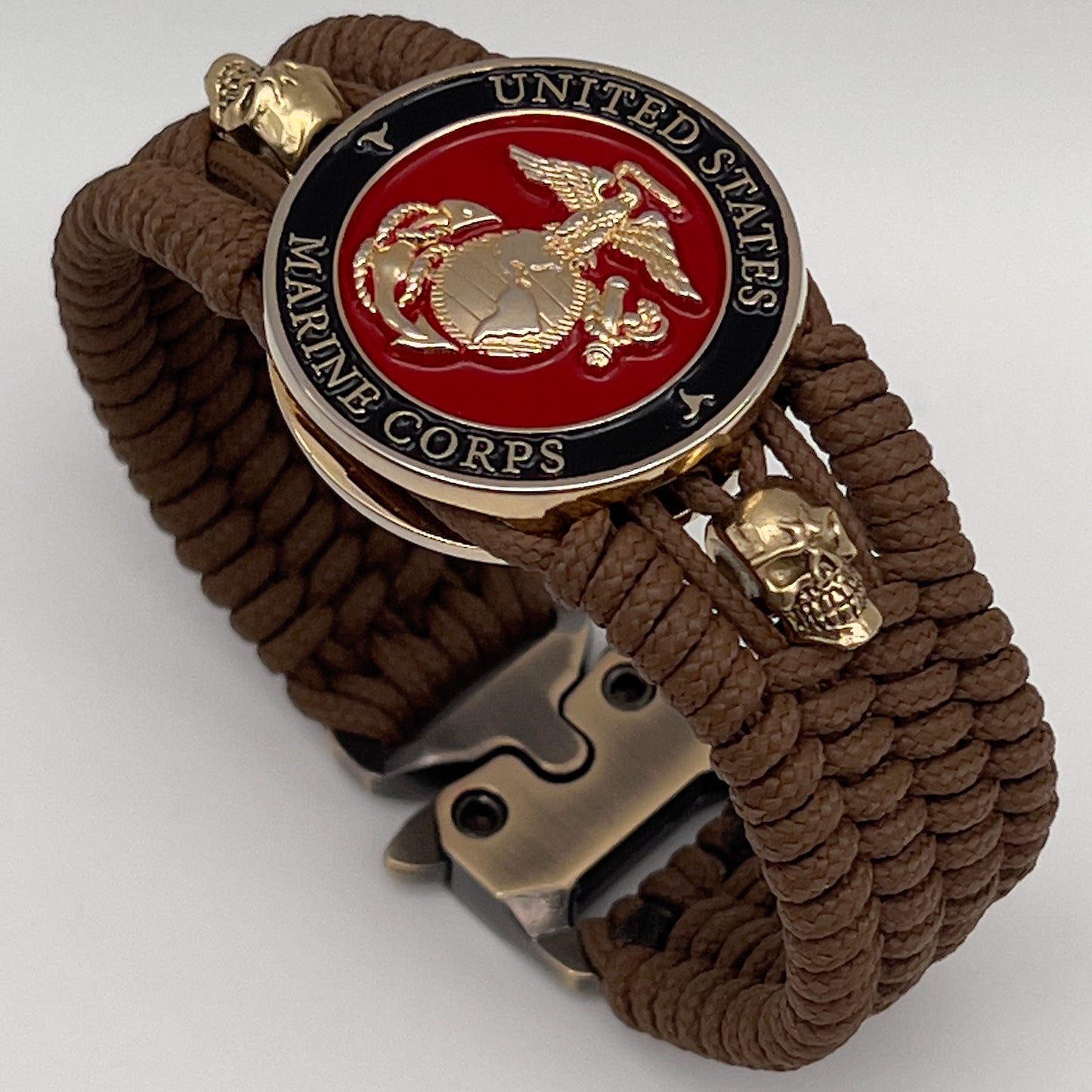 Thin, medium width, flexible and comfortable braided United States Marine Corps bracelet featuring a 24K gold plated USMC officer Eagle Globe and Anchor medallion, two gold plated skulls, a gold Cobra style tactical buckle and woven with Coyote Brown Type-1 paracord.