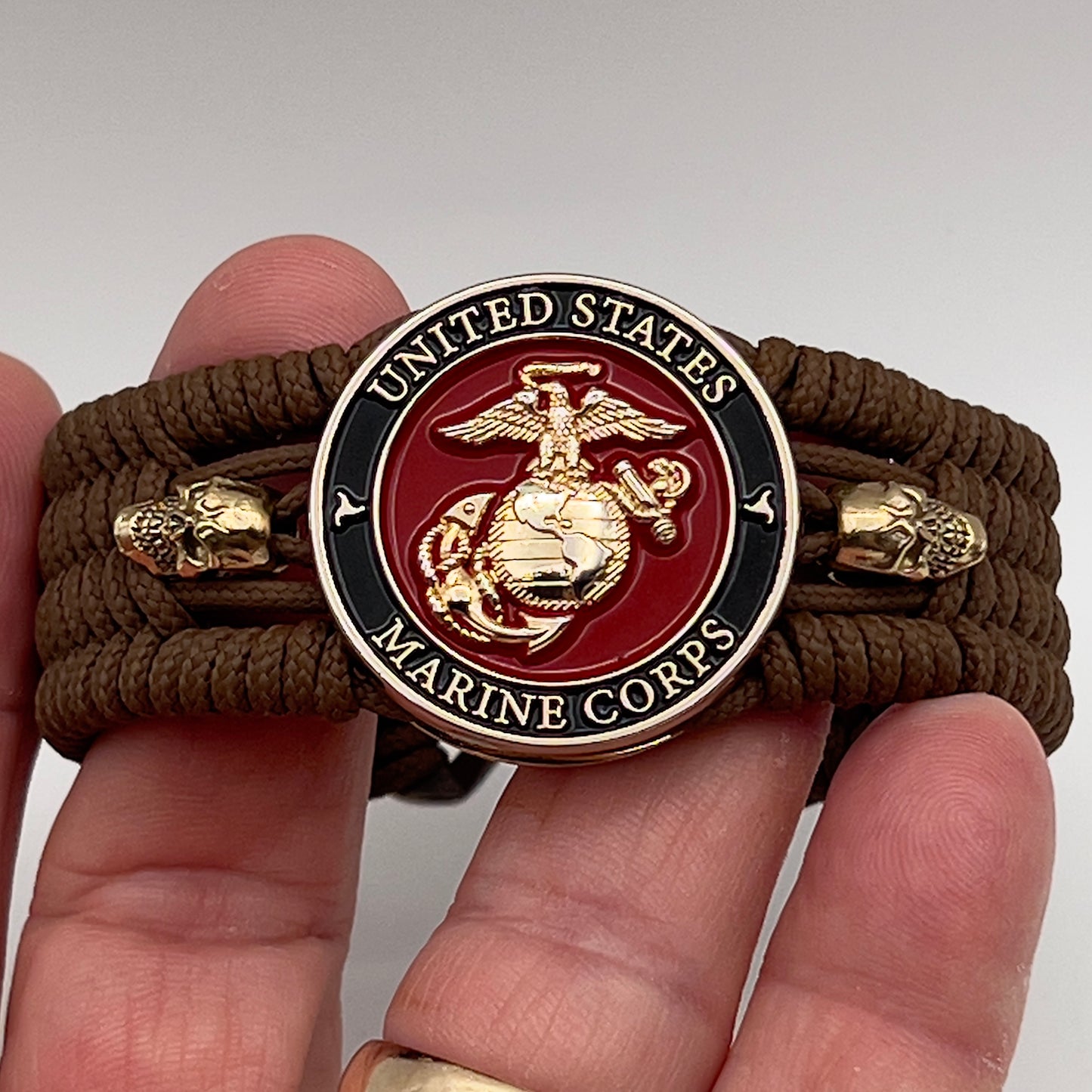 Thin, medium width, flexible and comfortable braided United States Marine Corps bracelet featuring a 24K gold plated USMC officer Eagle Globe and Anchor medallion, two gold plated skulls, a gold Cobra style tactical buckle and woven with Coyote Brown Type-1 paracord.