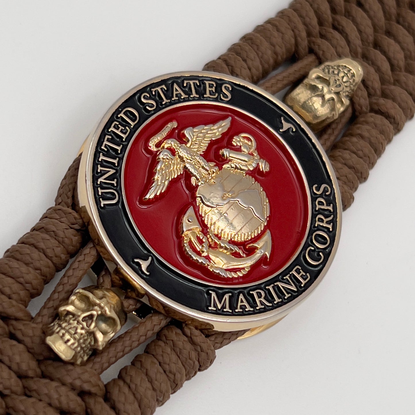 Thin, medium width, flexible and comfortable braided United States Marine Corps bracelet featuring a 24K gold plated USMC officer Eagle Globe and Anchor medallion, two gold plated skulls, a gold Cobra style tactical buckle and woven with Coyote Brown Type-1 paracord.