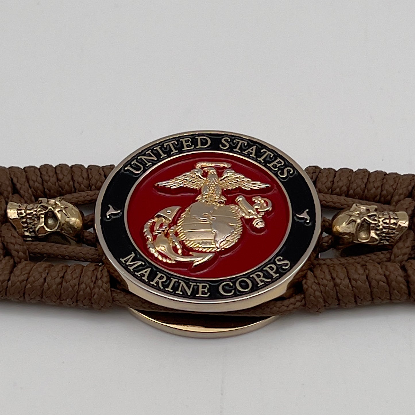 Thin, medium width, flexible and comfortable braided United States Marine Corps bracelet featuring a 24K gold plated USMC officer Eagle Globe and Anchor medallion, two gold plated skulls, a gold Cobra style tactical buckle and woven with Coyote Brown Type-1 paracord.