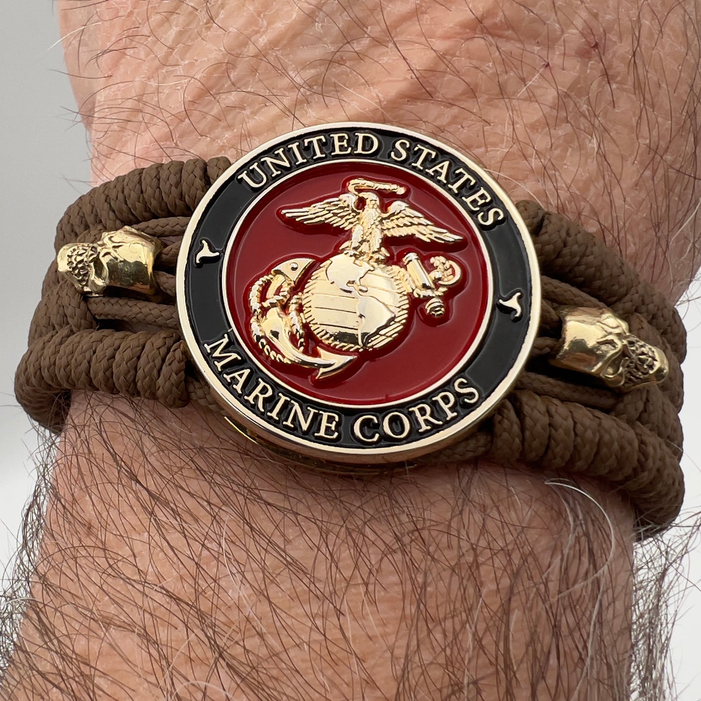 Thin, medium width, flexible and comfortable braided United States Marine Corps bracelet featuring a 24K gold plated USMC officer Eagle Globe and Anchor medallion, two gold plated skulls, a gold Cobra style tactical buckle and woven with Coyote Brown Type-1 paracord.