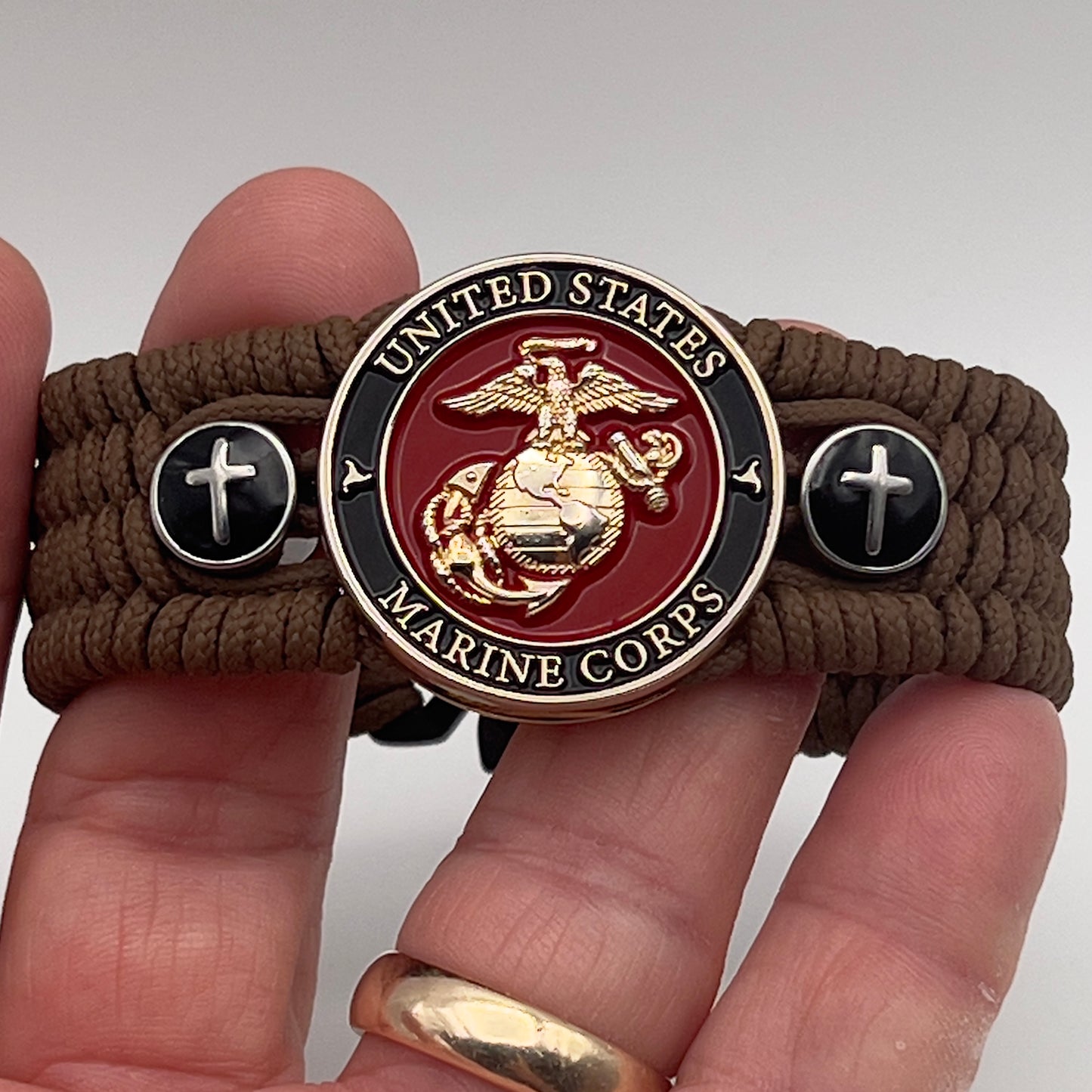 Thin, medium width, flexible and comfortable braided United States Marine Corps bracelet featuring a 24K gold plated USMC officer Eagle Globe and Anchor medallion, two Christian crosses, a black Cobra style tactical buckle and woven with Coyote Brown Type-1 paracord.