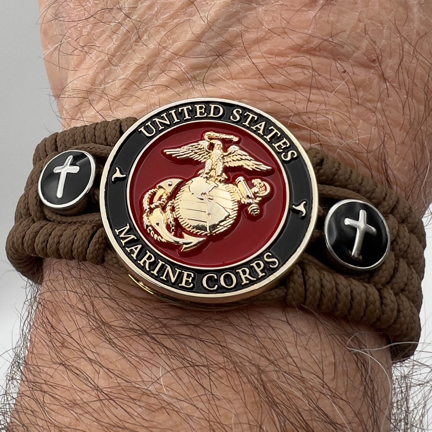Thin, medium width, flexible and comfortable braided United States Marine Corps bracelet featuring a 24K gold plated USMC officer Eagle Globe and Anchor medallion, two Christian crosses, a black Cobra style tactical buckle and woven with Coyote Brown Type-1 paracord.