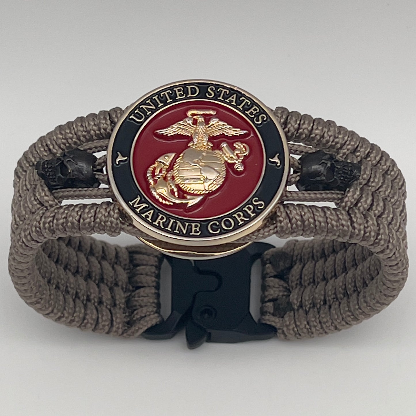 Thin, medium width, flexible and comfortable braided United States Marine Corps bracelet featuring a 24K gold plated USMC officer Eagle Globe and Anchor medallion, two black skulls, a black Cobra style tactical buckle and woven with tan Type-1 paracord.