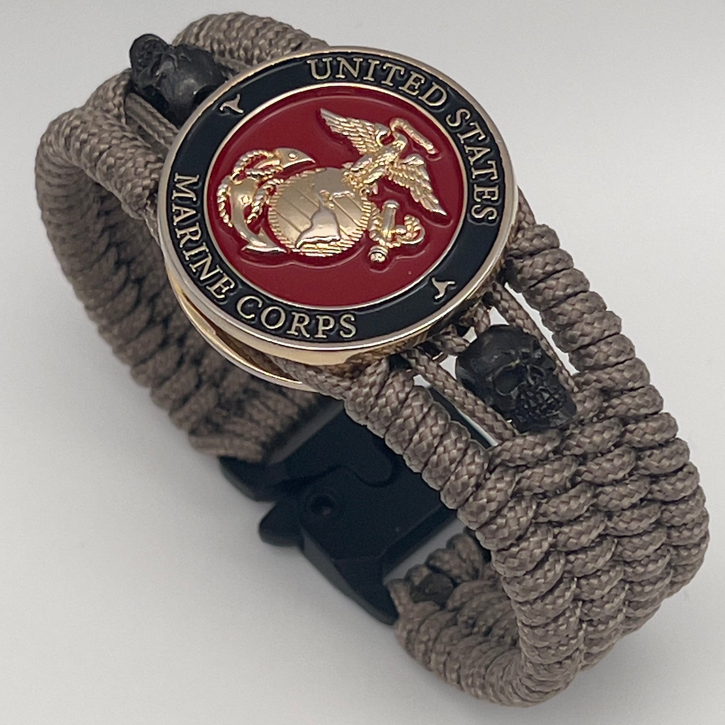 Thin, medium width, flexible and comfortable braided United States Marine Corps bracelet featuring a 24K gold plated USMC officer Eagle Globe and Anchor medallion, two black skulls, a black Cobra style tactical buckle and woven with tan Type-1 paracord.
