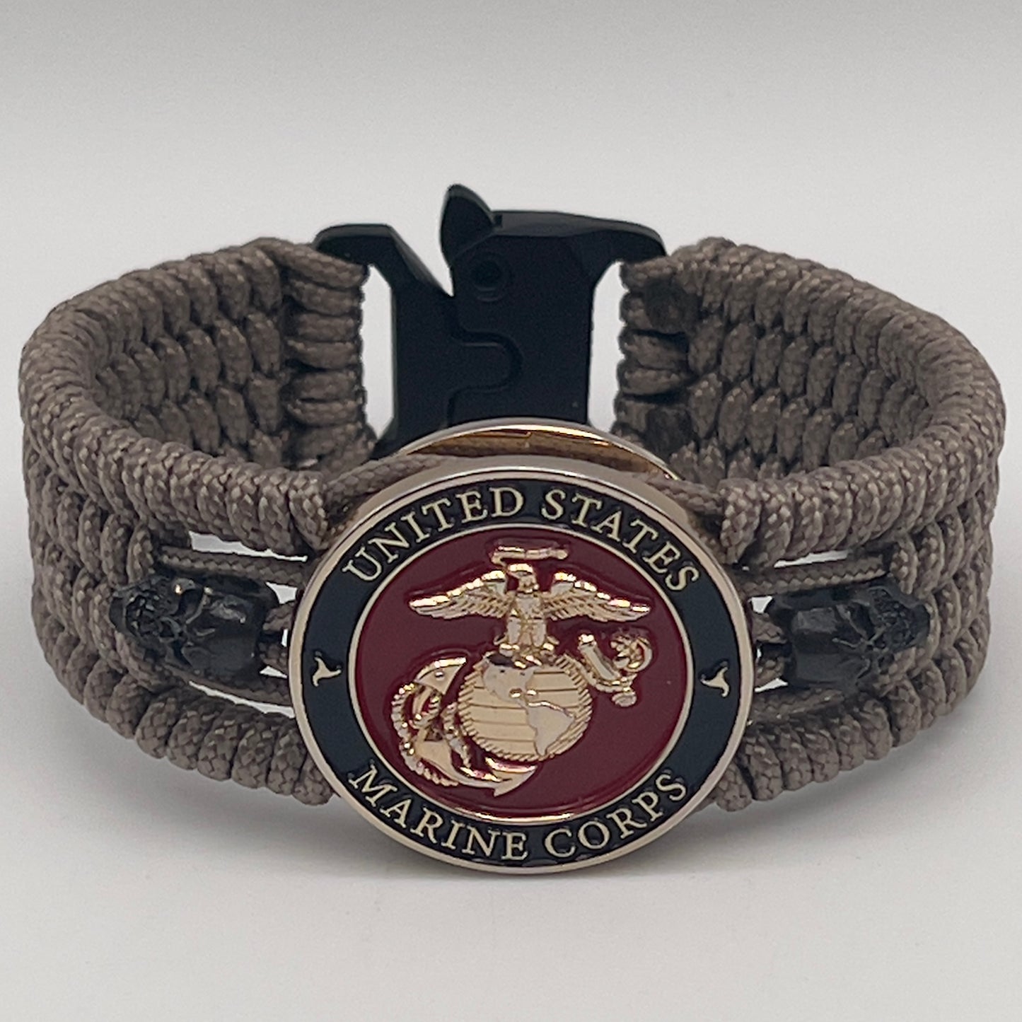 Thin, medium width, flexible and comfortable braided United States Marine Corps bracelet featuring a 24K gold plated USMC officer Eagle Globe and Anchor medallion, two black skulls, a black Cobra style tactical buckle and woven with tan Type-1 paracord.