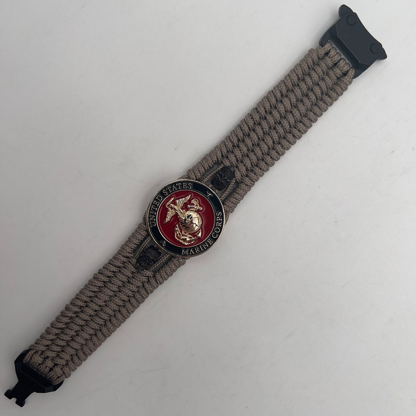 Thin, medium width, flexible and comfortable braided United States Marine Corps bracelet featuring a 24K gold plated USMC officer Eagle Globe and Anchor medallion, two black skulls, a black Cobra style tactical buckle and woven with tan Type-1 paracord.