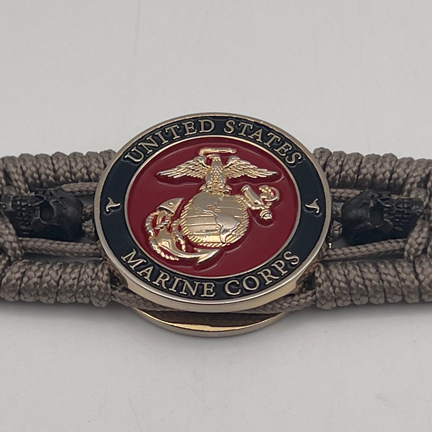 Thin, medium width, flexible and comfortable braided United States Marine Corps bracelet featuring a 24K gold plated USMC officer Eagle Globe and Anchor medallion, two black skulls, a black Cobra style tactical buckle and woven with tan Type-1 paracord.