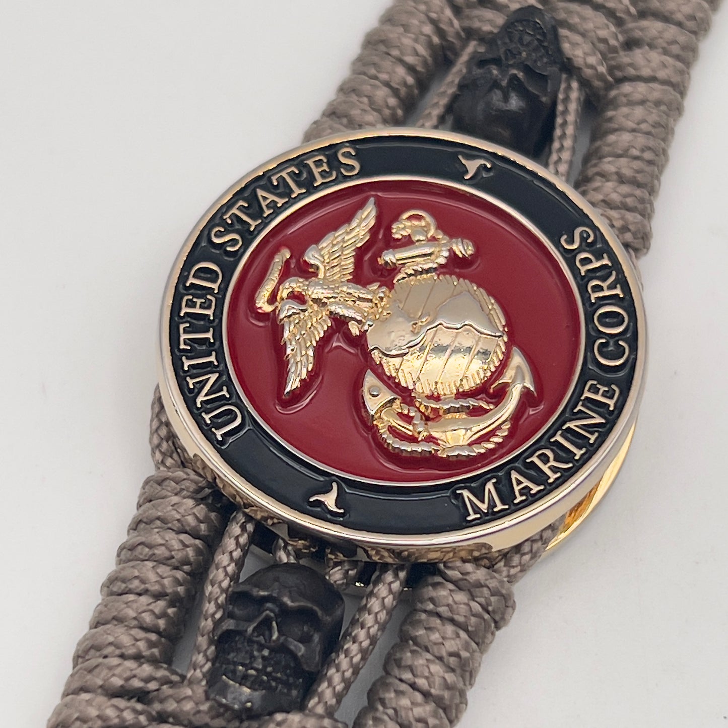 Thin, medium width, flexible and comfortable braided United States Marine Corps bracelet featuring a 24K gold plated USMC officer Eagle Globe and Anchor medallion, two black skulls, a black Cobra style tactical buckle and woven with tan Type-1 paracord.