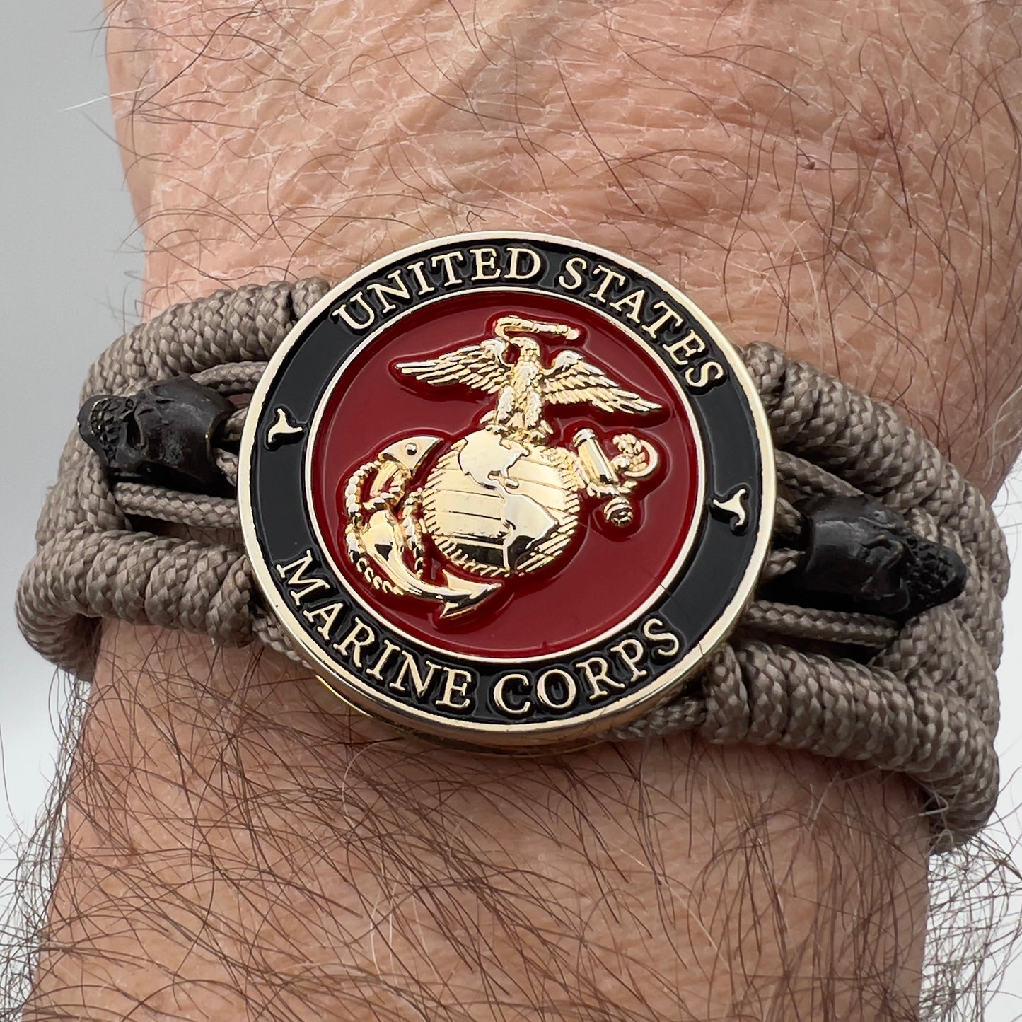 Thin, medium width, flexible and comfortable braided United States Marine Corps bracelet featuring a 24K gold plated USMC officer Eagle Globe and Anchor medallion, two black skulls, a black Cobra style tactical buckle and woven with tan Type-1 paracord.