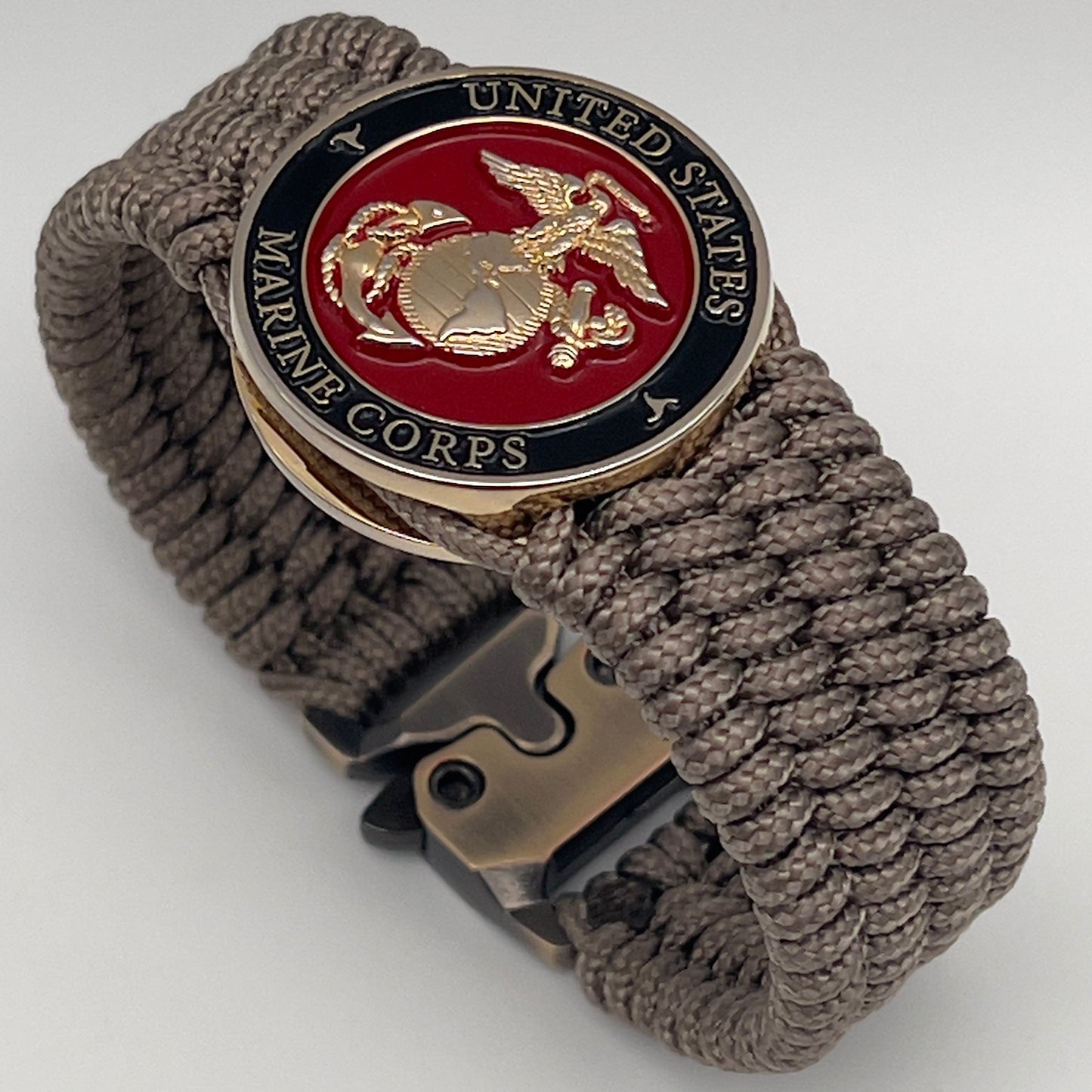 Thin, medium width, flexible and comfortable braided United States Marine Corps bracelet featuring a 24K gold plated USMC officer Eagle Globe and Anchor medallion, a gold Cobra style tactical buckle and woven with Tan Type-1 paracord.
