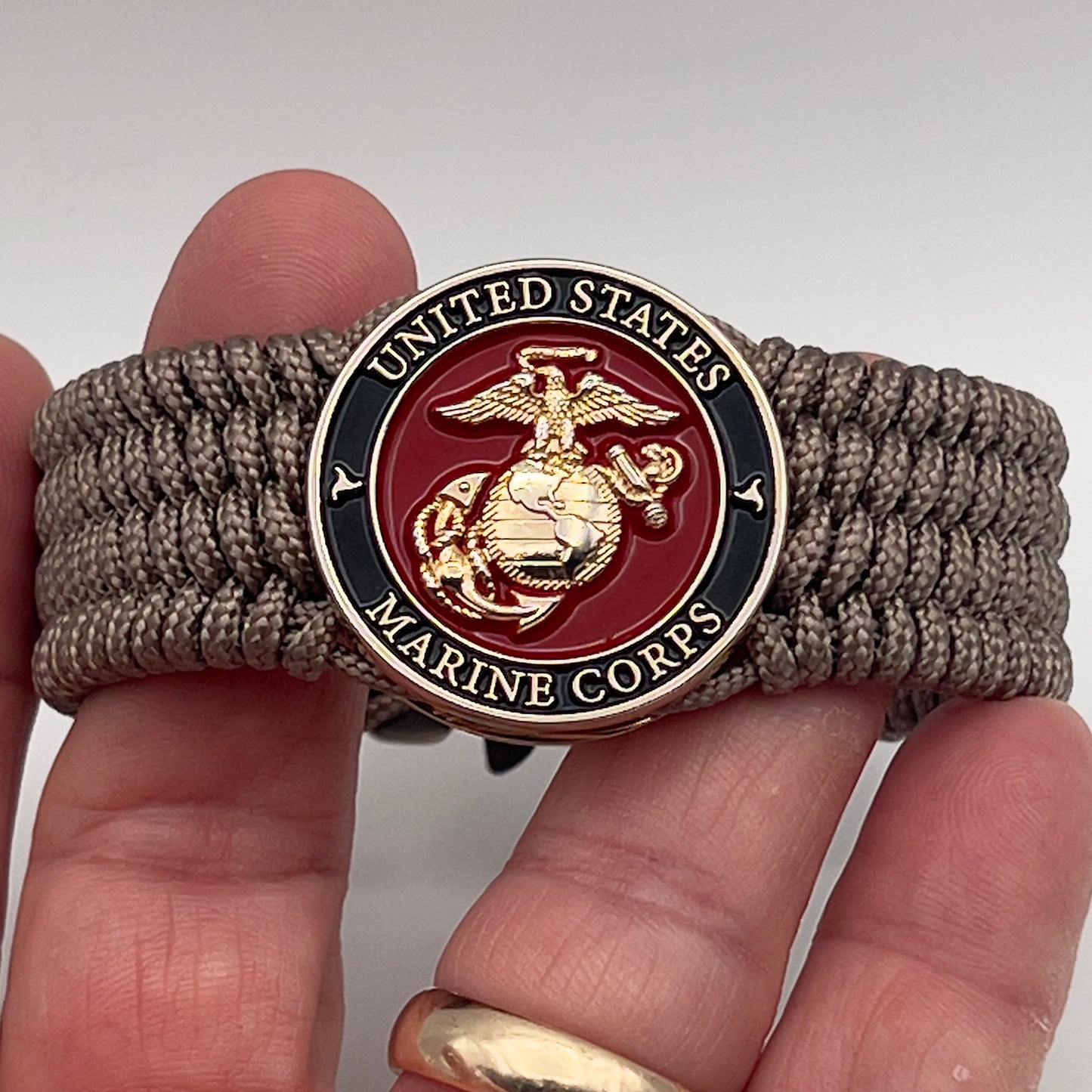 Thin, medium width, flexible and comfortable braided United States Marine Corps bracelet featuring a 24K gold plated USMC officer Eagle Globe and Anchor medallion, a gold Cobra style tactical buckle and woven with Tan Type-1 paracord.