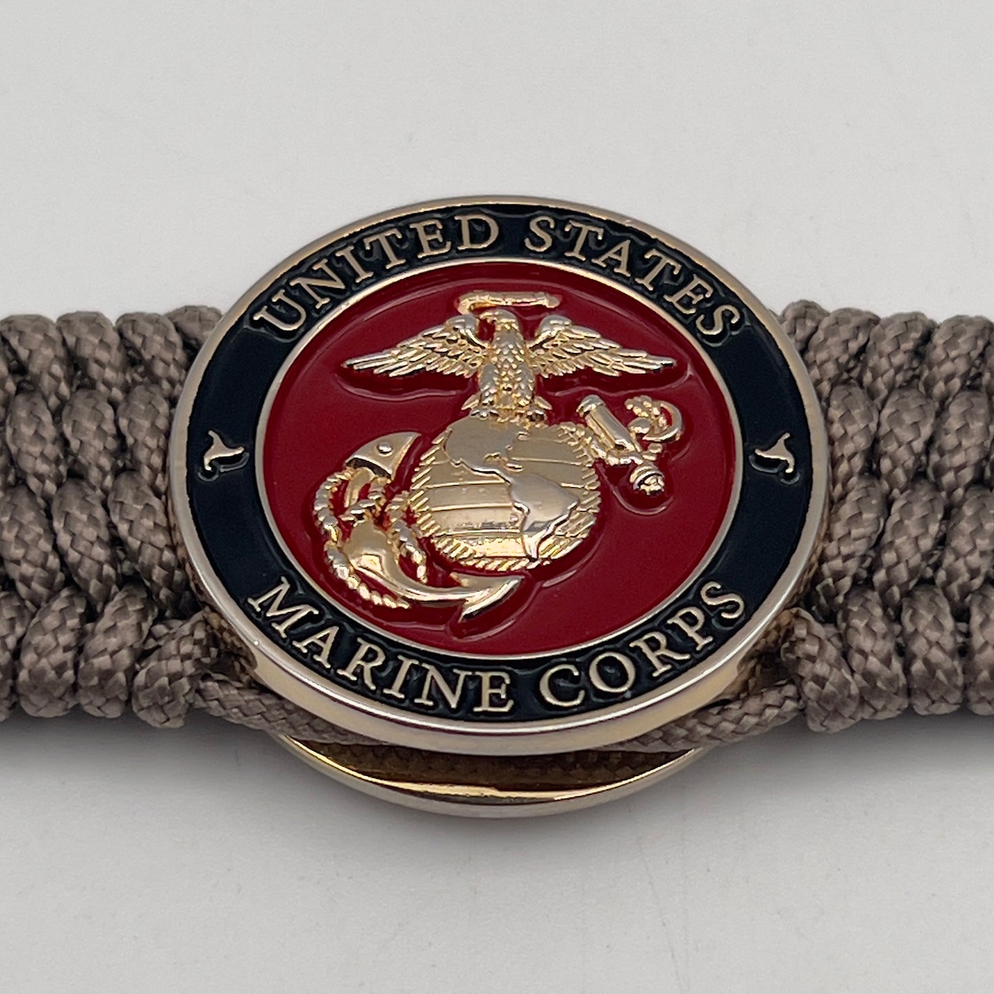 Thin, medium width, flexible and comfortable braided United States Marine Corps bracelet featuring a 24K gold plated USMC officer Eagle Globe and Anchor medallion, a gold Cobra style tactical buckle and woven with Tan Type-1 paracord.