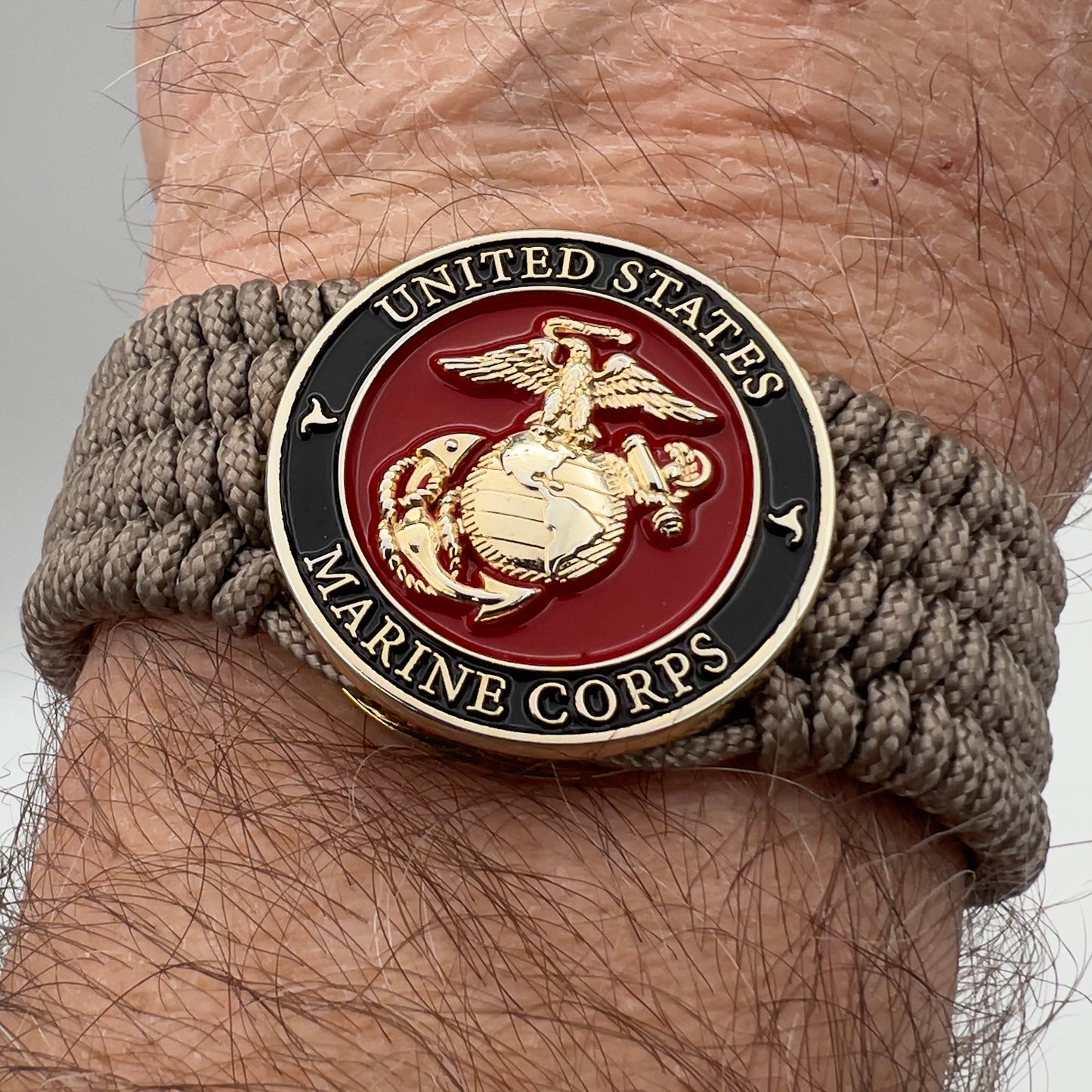 Thin, medium width, flexible and comfortable braided United States Marine Corps bracelet featuring a 24K gold plated USMC officer Eagle Globe and Anchor medallion, a gold Cobra style tactical buckle and woven with Tan Type-1 paracord.