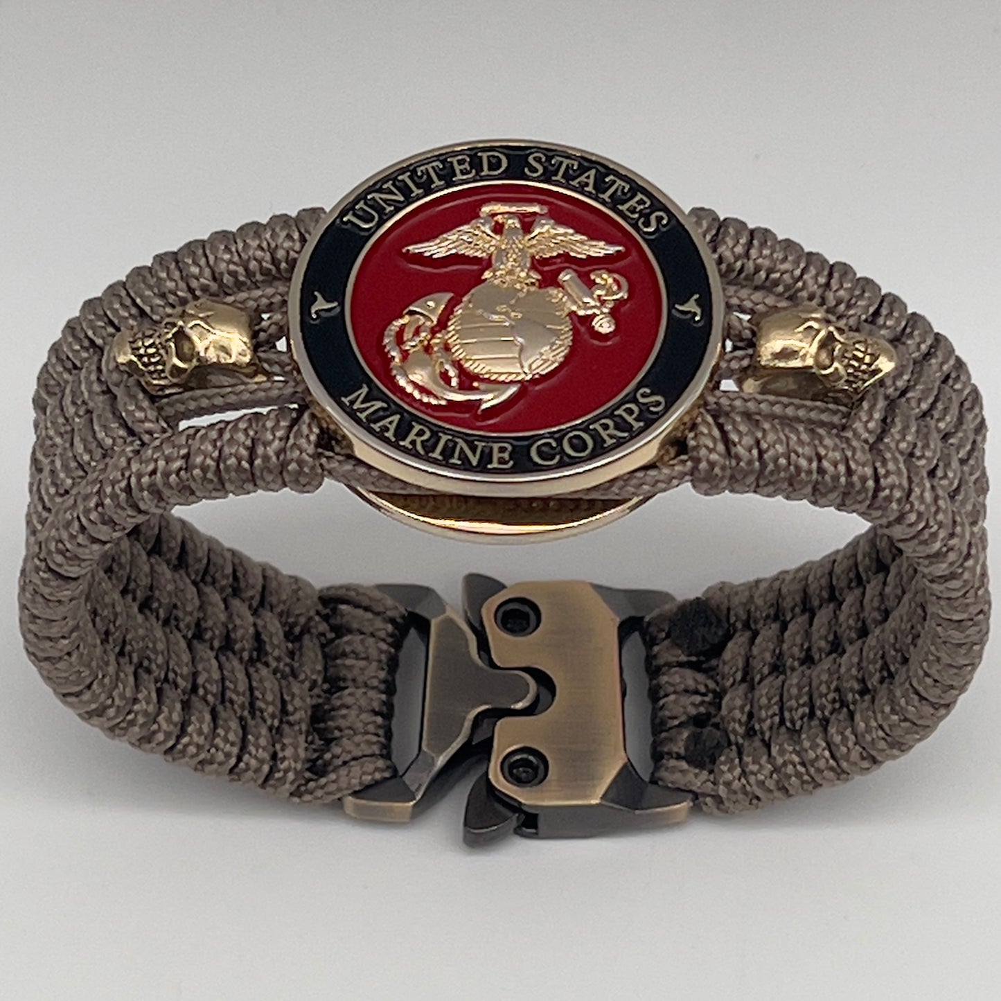 Thin, medium width, flexible and comfortable braided United States Marine Corps bracelet featuring a 24K gold plated USMC officer Eagle Globe and Anchor medallion, two gold plated skulls, a gold Cobra style tactical buckle and woven with Tan Type-1 paracord.