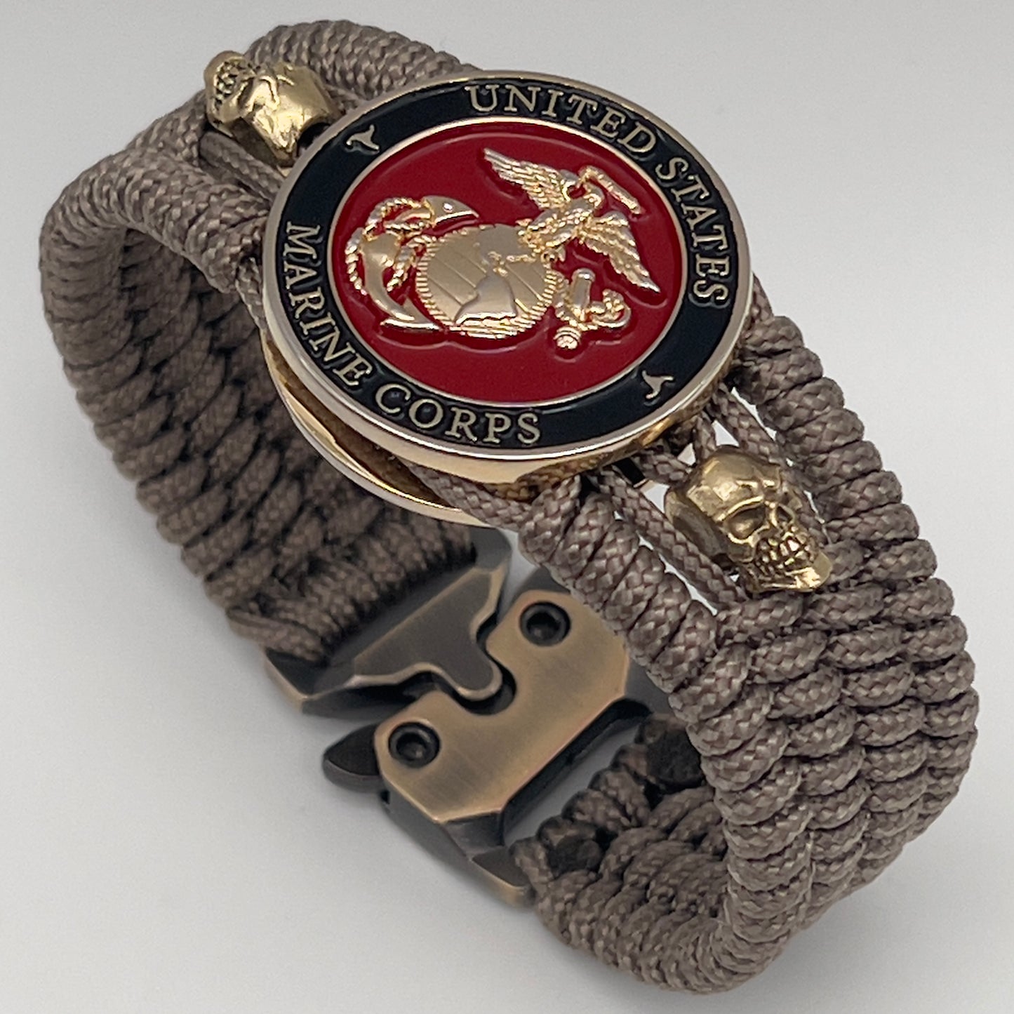 Thin, medium width, flexible and comfortable braided United States Marine Corps bracelet featuring a 24K gold plated USMC officer Eagle Globe and Anchor medallion, two gold plated skulls, a gold Cobra style tactical buckle and woven with Tan Type-1 paracord.