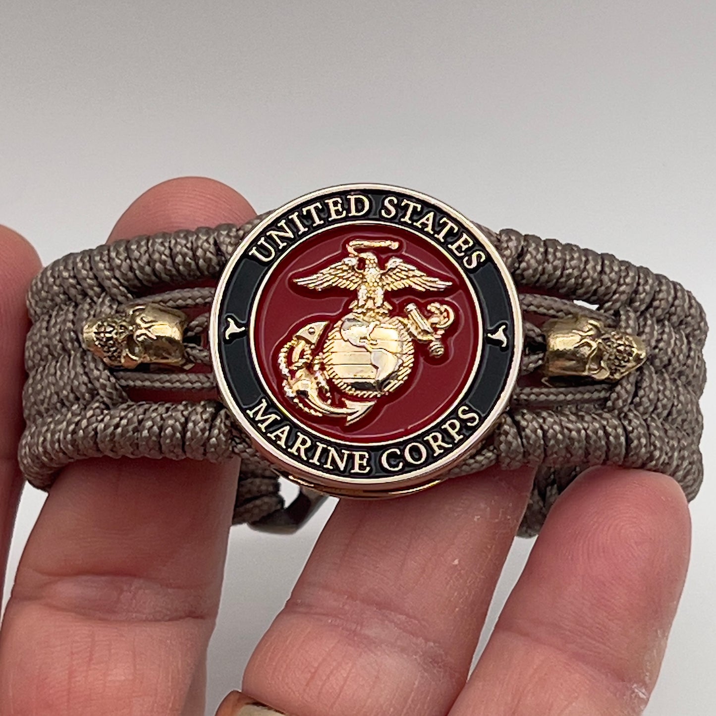 Thin, medium width, flexible and comfortable braided United States Marine Corps bracelet featuring a 24K gold plated USMC officer Eagle Globe and Anchor medallion, two gold plated skulls, a gold Cobra style tactical buckle and woven with Tan Type-1 paracord.