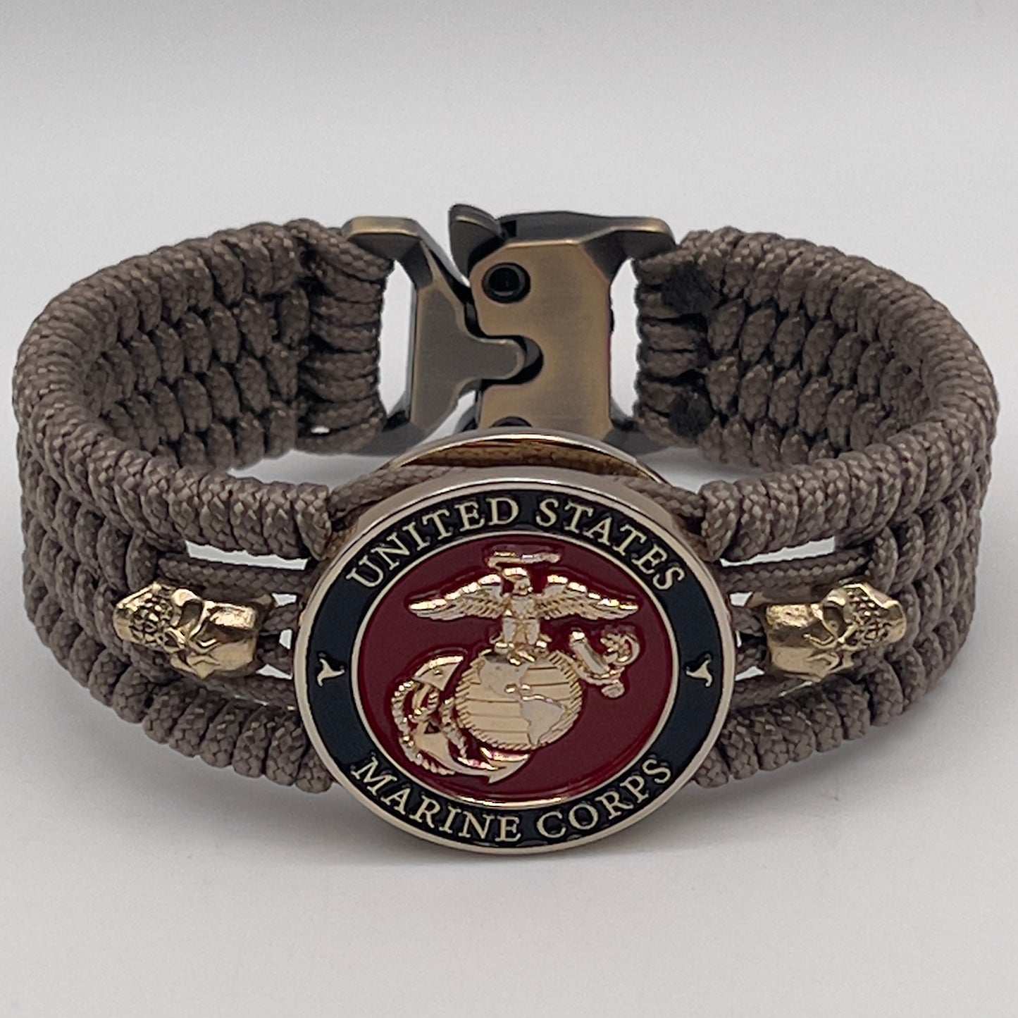 Thin, medium width, flexible and comfortable braided United States Marine Corps bracelet featuring a 24K gold plated USMC officer Eagle Globe and Anchor medallion, two gold plated skulls, a gold Cobra style tactical buckle and woven with Tan Type-1 paracord.