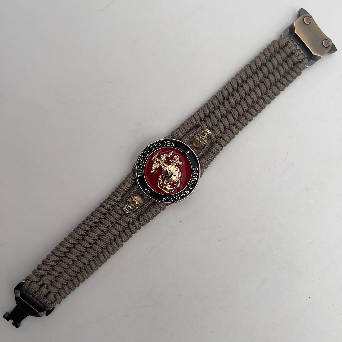 Thin, medium width, flexible and comfortable braided United States Marine Corps bracelet featuring a 24K gold plated USMC officer Eagle Globe and Anchor medallion, two gold plated skulls, a gold Cobra style tactical buckle and woven with Tan Type-1 paracord.