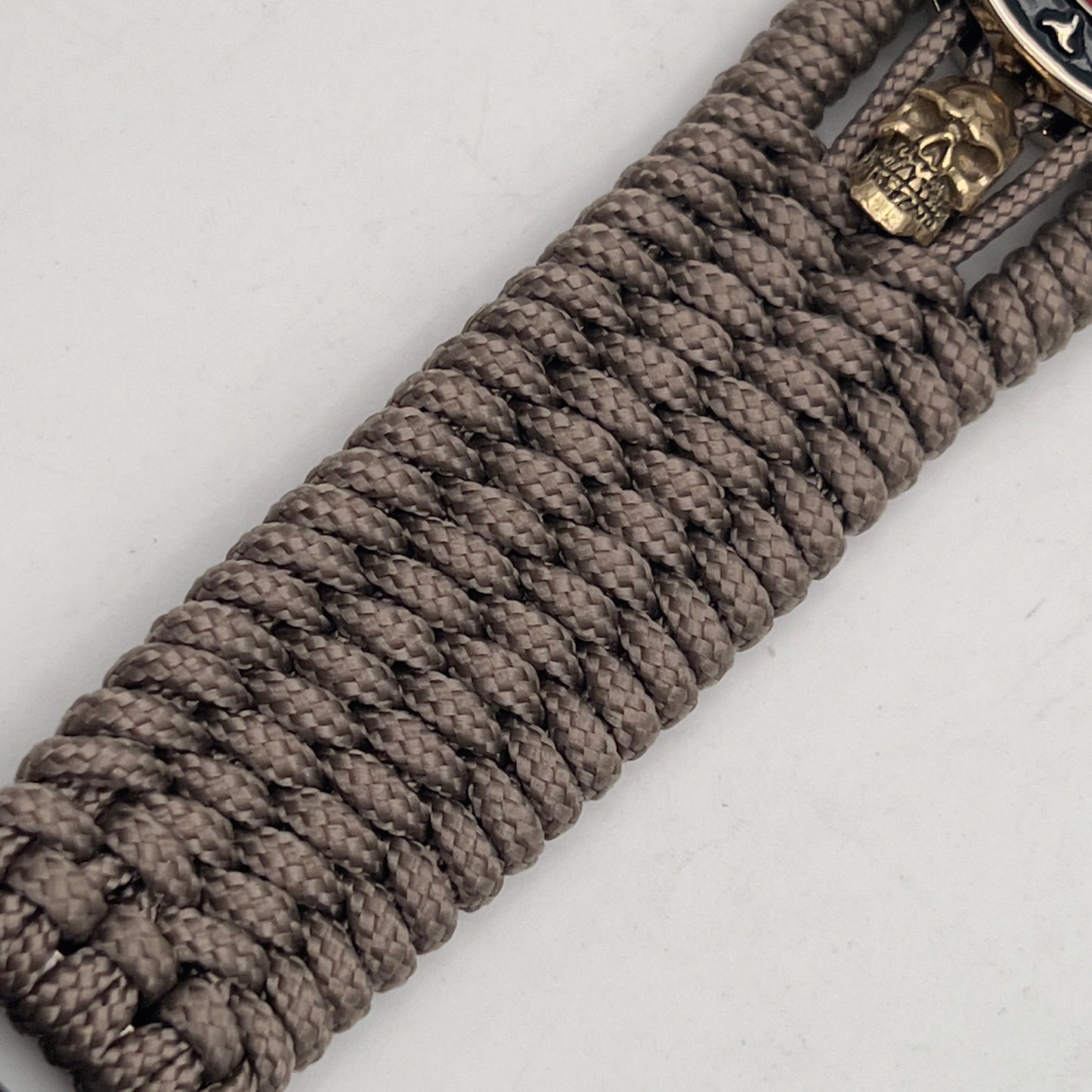 Thin, medium width, flexible and comfortable braided United States Marine Corps bracelet featuring a 24K gold plated USMC officer Eagle Globe and Anchor medallion, two gold plated skulls, a gold Cobra style tactical buckle and woven with Tan Type-1 paracord.