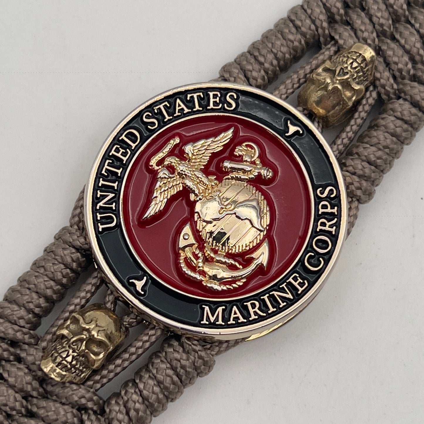 Thin, medium width, flexible and comfortable braided United States Marine Corps bracelet featuring a 24K gold plated USMC officer Eagle Globe and Anchor medallion, two gold plated skulls, a gold Cobra style tactical buckle and woven with Tan Type-1 paracord.