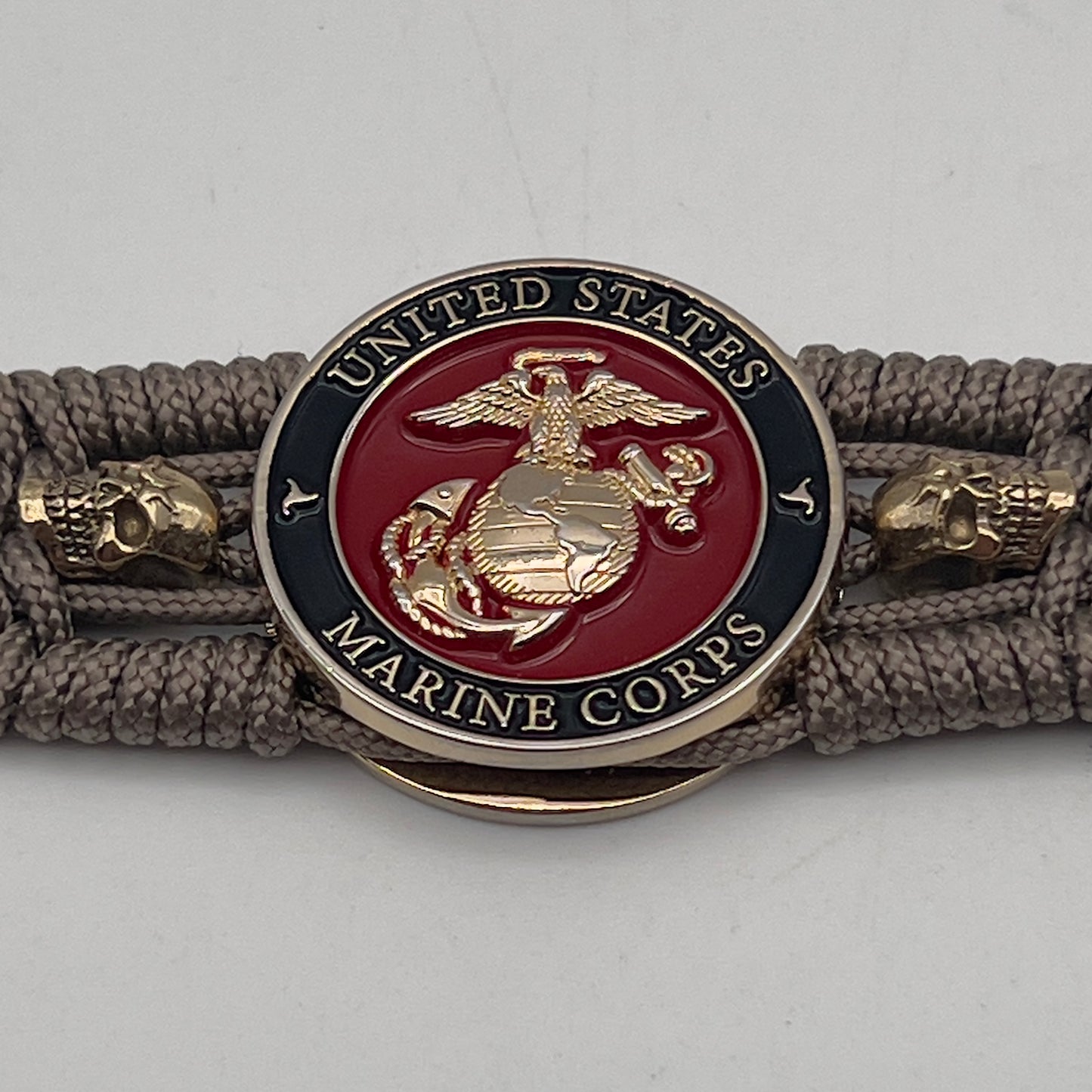 Thin, medium width, flexible and comfortable braided United States Marine Corps bracelet featuring a 24K gold plated USMC officer Eagle Globe and Anchor medallion, two gold plated skulls, a gold Cobra style tactical buckle and woven with Tan Type-1 paracord.