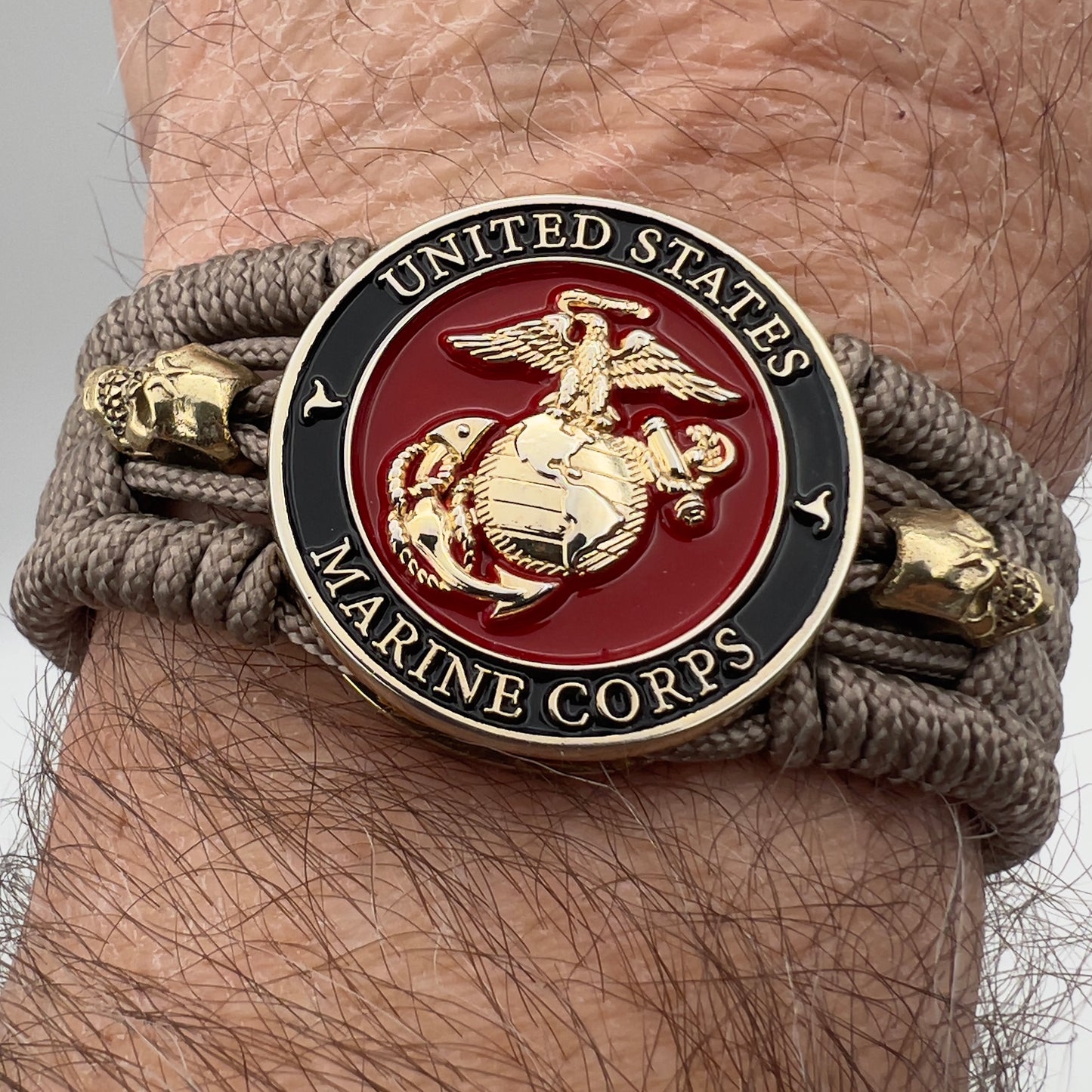 Thin, medium width, flexible and comfortable braided United States Marine Corps bracelet featuring a 24K gold plated USMC officer Eagle Globe and Anchor medallion, two gold plated skulls, a gold Cobra style tactical buckle and woven with Tan Type-1 paracord.