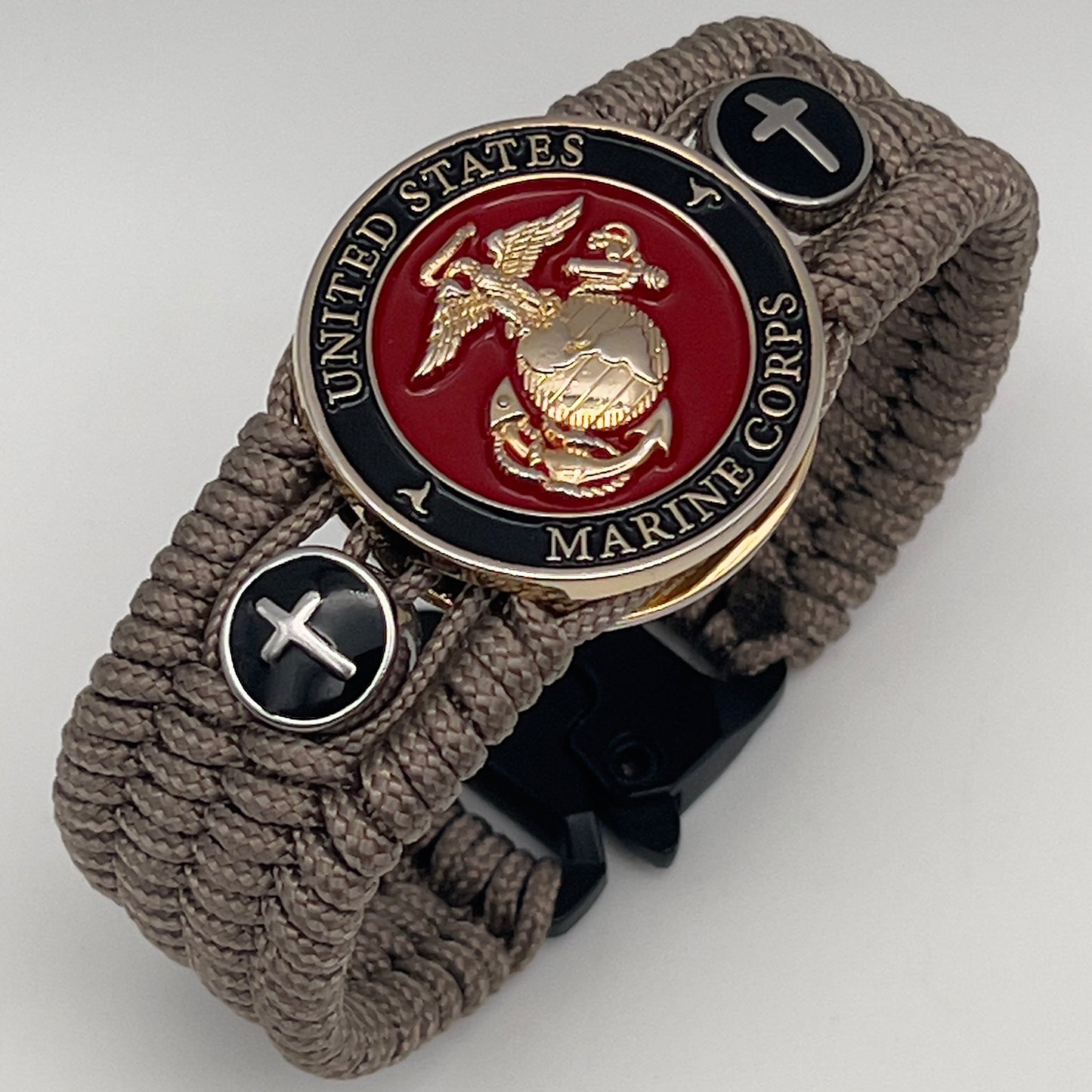 Thin, medium width, flexible and comfortable braided United States Marine Corps bracelet featuring a 24K gold plated USMC officer Eagle Globe and Anchor medallion, two Christian crosses, a black Cobra style tactical buckle and woven with Tan Type-1 paracord.