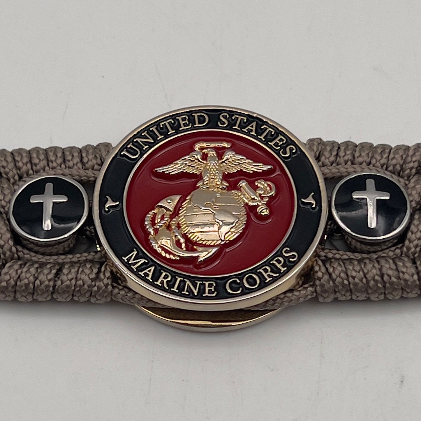Thin, medium width, flexible and comfortable braided United States Marine Corps bracelet featuring a 24K gold plated USMC officer Eagle Globe and Anchor medallion, two Christian crosses, a black Cobra style tactical buckle and woven with Tan Type-1 paracord.