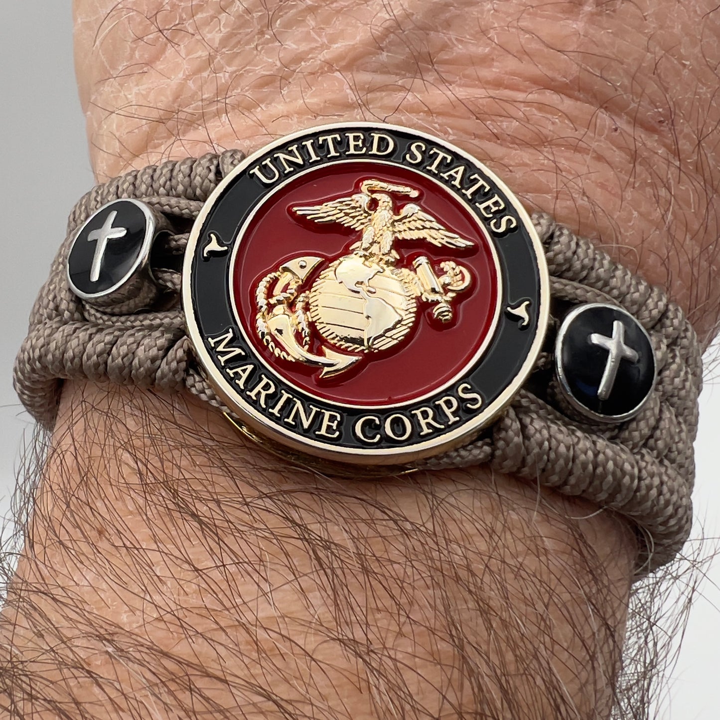 Thin, medium width, flexible and comfortable braided United States Marine Corps bracelet featuring a 24K gold plated USMC officer Eagle Globe and Anchor medallion, two Christian crosses, a black Cobra style tactical buckle and woven with Tan Type-1 paracord.