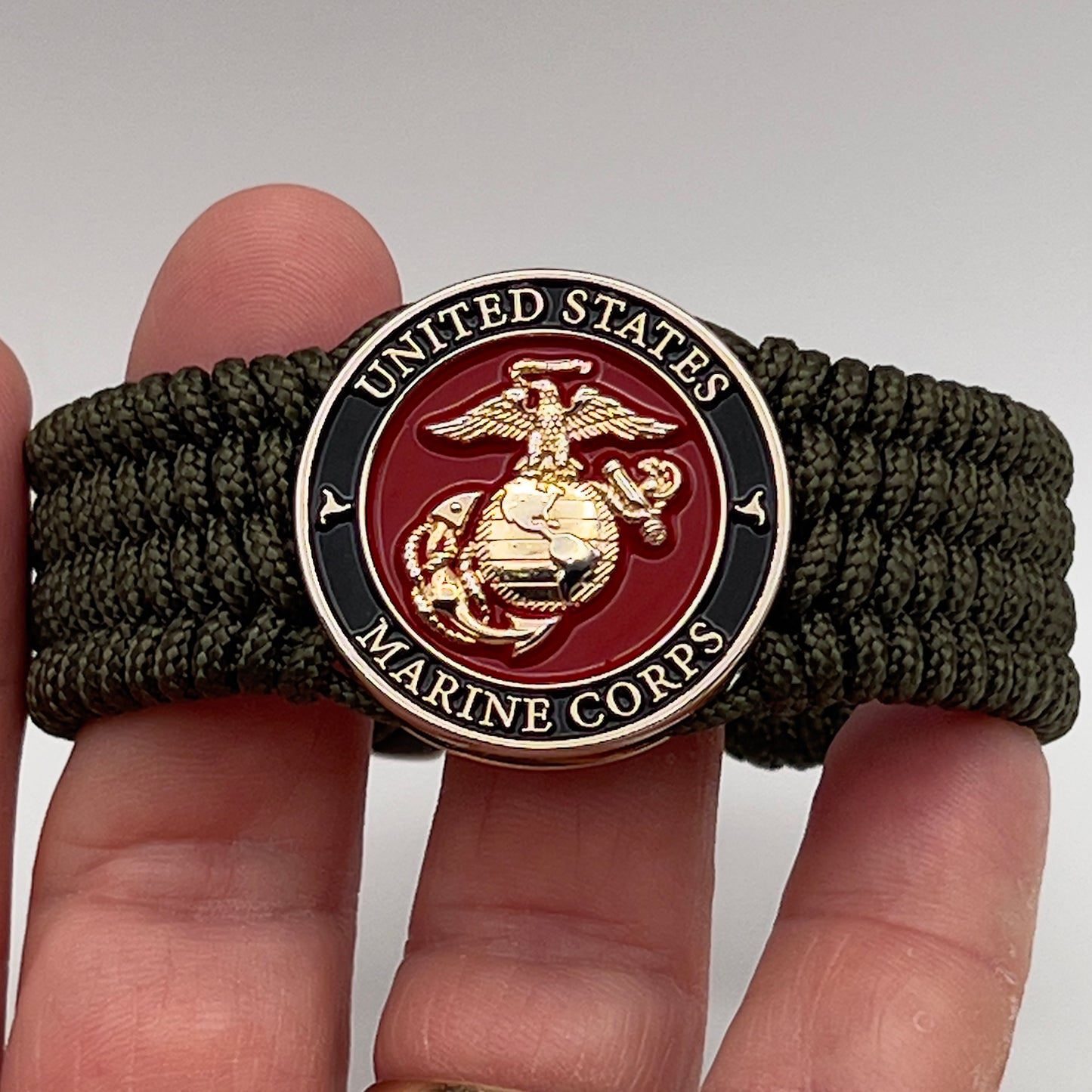 Thin, medium width, flexible and comfortable braided United States Marine Corps bracelet featuring a 24K gold plated USMC officer Eagle Globe and Anchor medallion, a gold Cobra style tactical buckle and woven with Olive Drab Type-1 paracord.