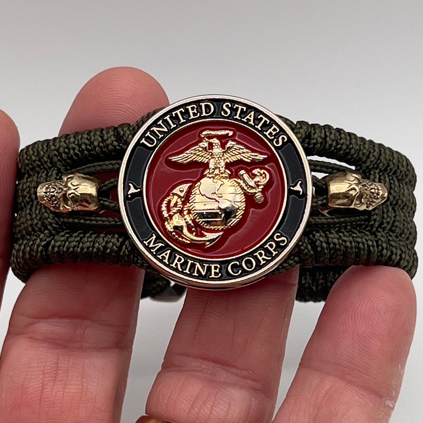 Thin, medium width, flexible and comfortable braided United States Marine Corps bracelet featuring a 24K gold plated USMC officer Eagle Globe and Anchor medallion, two gold plated skulls, a gold Cobra style tactical buckle and woven with Olive Drab Type-1 paracord.