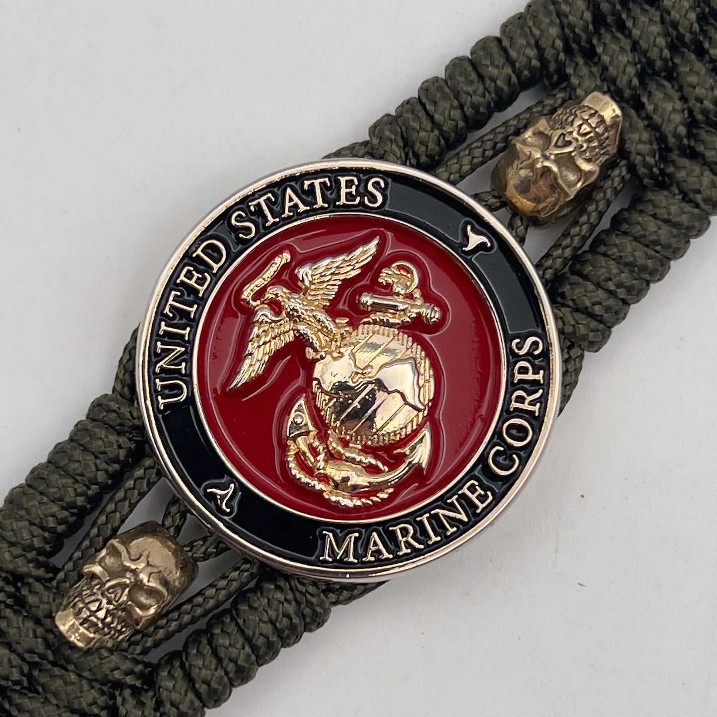 Thin, medium width, flexible and comfortable braided United States Marine Corps bracelet featuring a 24K gold plated USMC officer Eagle Globe and Anchor medallion, two gold plated skulls, a gold Cobra style tactical buckle and woven with Olive Drab Type-1 paracord.