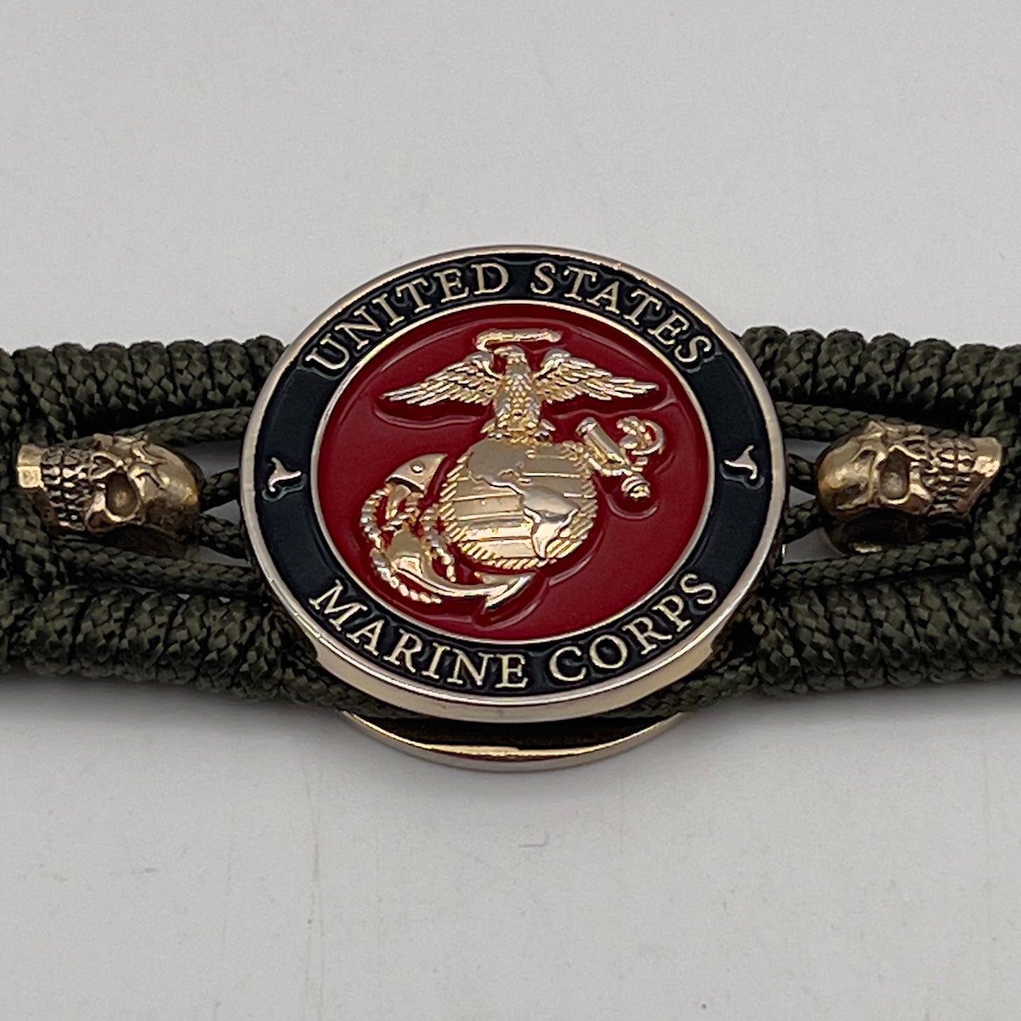 Thin, medium width, flexible and comfortable braided United States Marine Corps bracelet featuring a 24K gold plated USMC officer Eagle Globe and Anchor medallion, two gold plated skulls, a gold Cobra style tactical buckle and woven with Olive Drab Type-1 paracord.