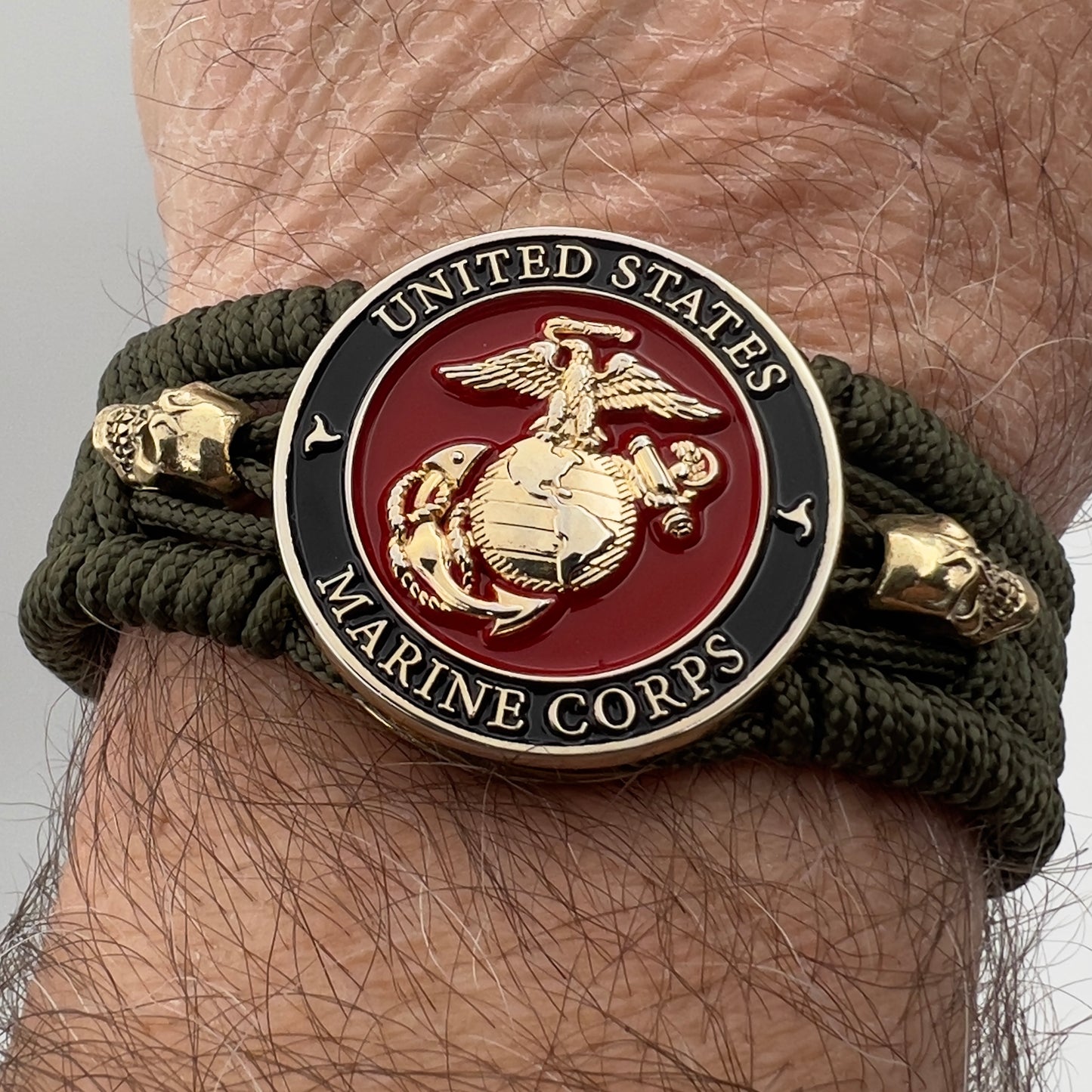 Thin, medium width, flexible and comfortable braided United States Marine Corps bracelet featuring a 24K gold plated USMC officer Eagle Globe and Anchor medallion, two gold plated skulls, a gold Cobra style tactical buckle and woven with Olive Drab Type-1 paracord.
