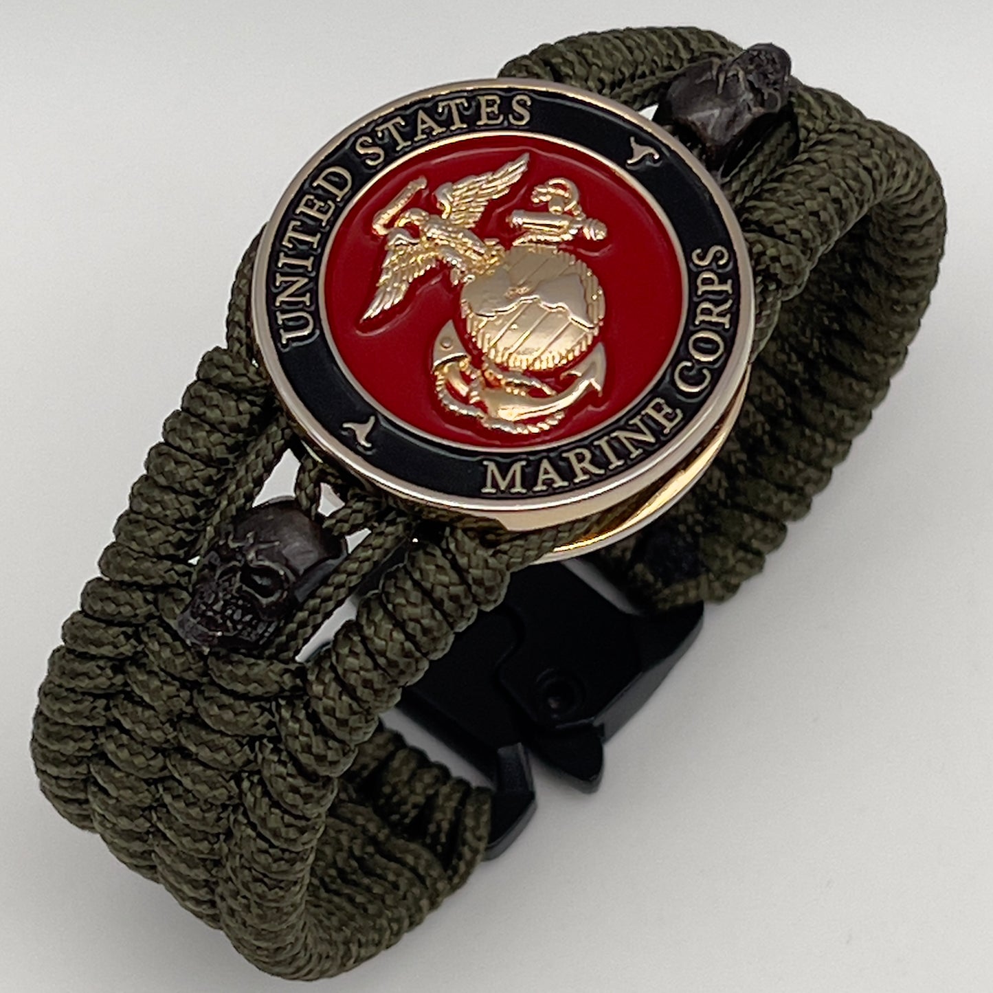 Thin, medium width, flexible and comfortable braided United States Marine Corps bracelet featuring a 24K gold plated USMC officer Eagle Globe and Anchor medallion, two black micro skulls, a black Cobra style tactical buckle and woven with Olive Drab Type-1 paracord.