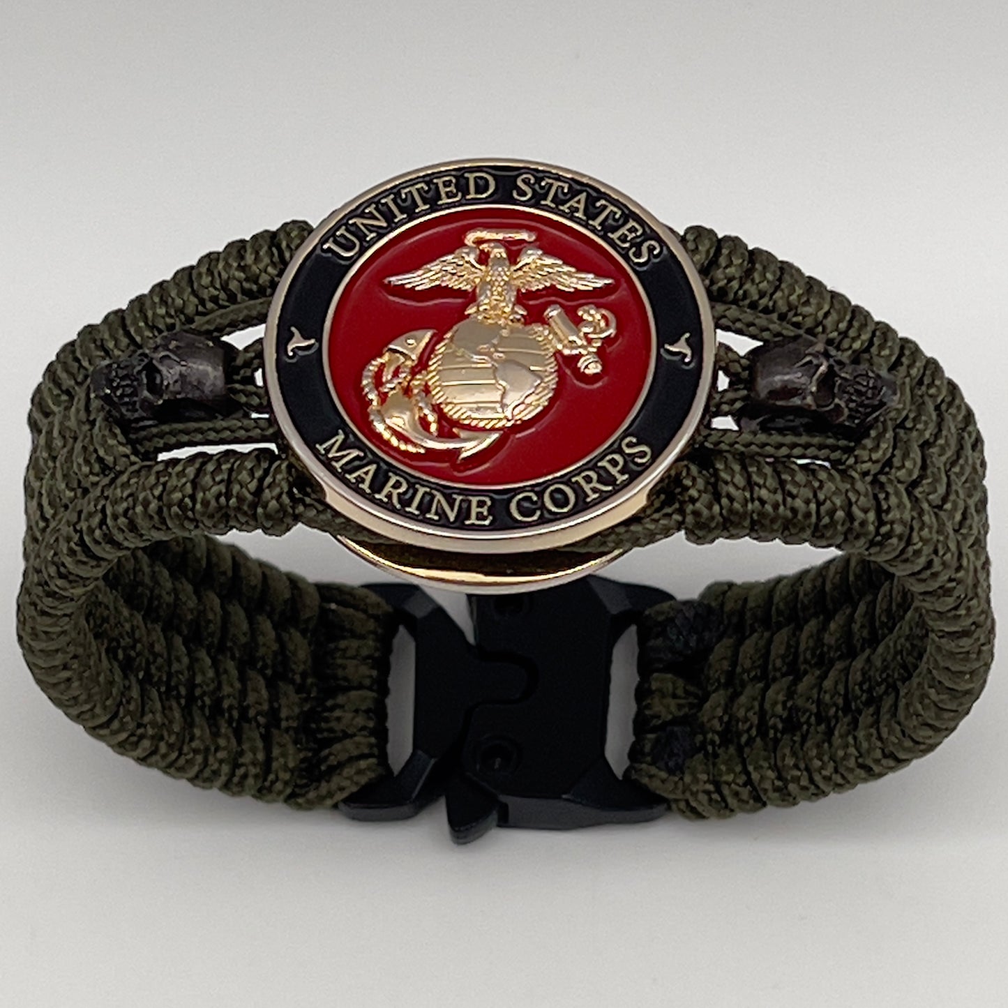 Thin, medium width, flexible and comfortable braided United States Marine Corps bracelet featuring a 24K gold plated USMC officer Eagle Globe and Anchor medallion, two black micro skulls, a black Cobra style tactical buckle and woven with Olive Drab Type-1 paracord.
