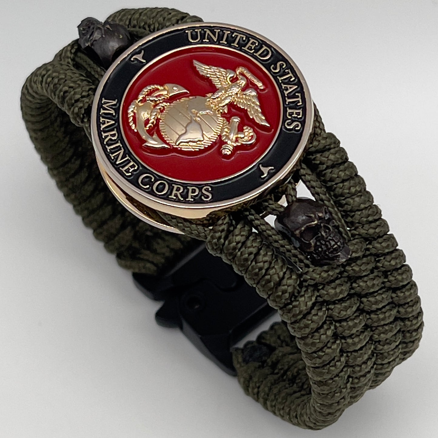 Thin, medium width, flexible and comfortable braided United States Marine Corps bracelet featuring a 24K gold plated USMC officer Eagle Globe and Anchor medallion, two black micro skulls, a black Cobra style tactical buckle and woven with Olive Drab Type-1 paracord.