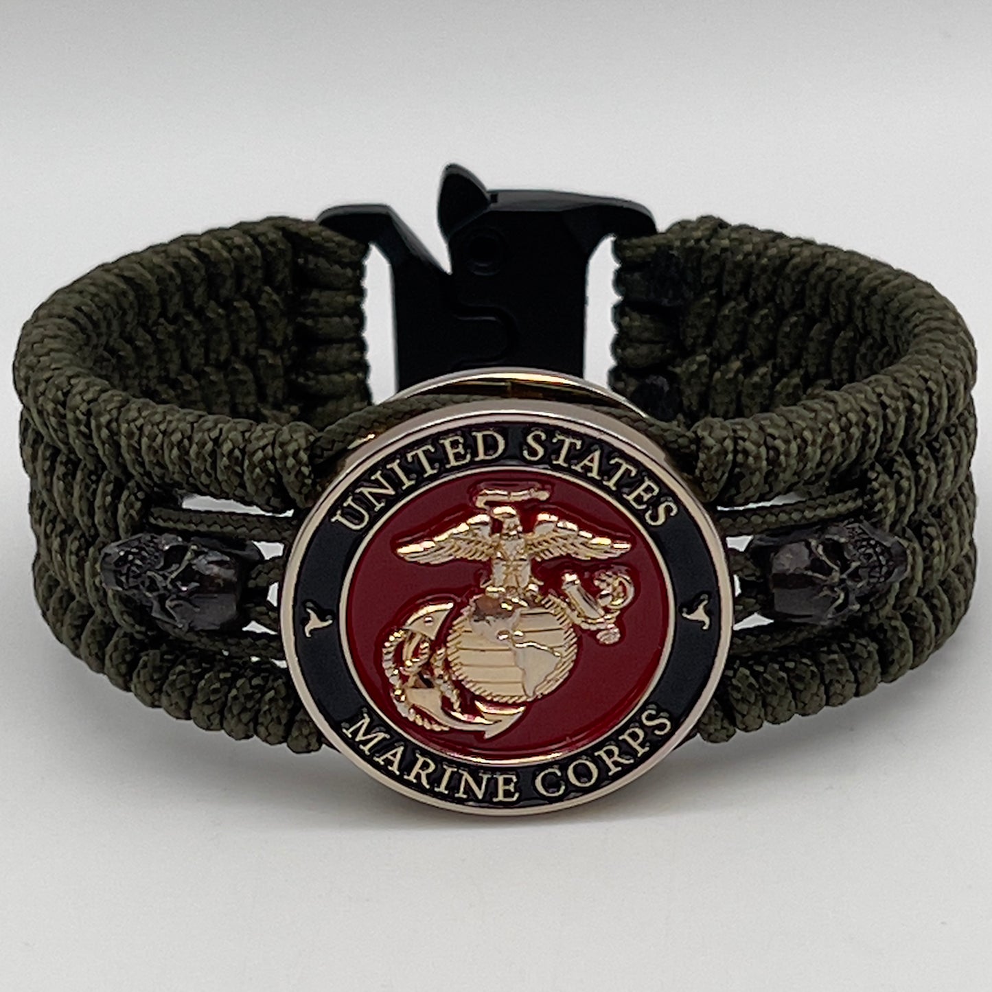 Thin, medium width, flexible and comfortable braided United States Marine Corps bracelet featuring a 24K gold plated USMC officer Eagle Globe and Anchor medallion, two black micro skulls, a black Cobra style tactical buckle and woven with Olive Drab Type-1 paracord.