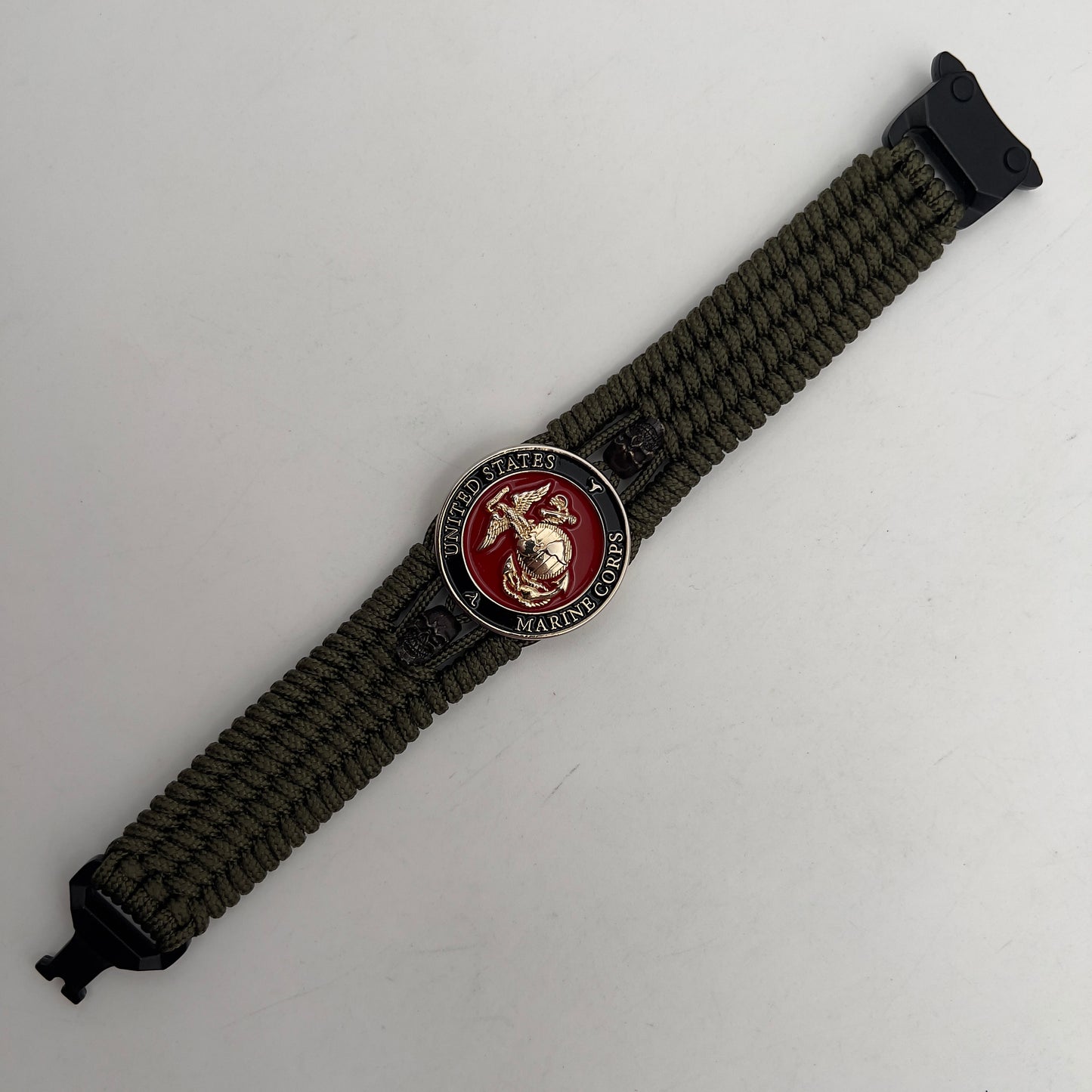 Thin, medium width, flexible and comfortable braided United States Marine Corps bracelet featuring a 24K gold plated USMC officer Eagle Globe and Anchor medallion, two black micro skulls, a black Cobra style tactical buckle and woven with Olive Drab Type-1 paracord.