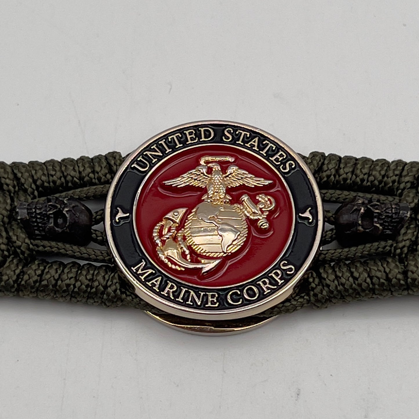 Thin, medium width, flexible and comfortable braided United States Marine Corps bracelet featuring a 24K gold plated USMC officer Eagle Globe and Anchor medallion, two black micro skulls, a black Cobra style tactical buckle and woven with Olive Drab Type-1 paracord.