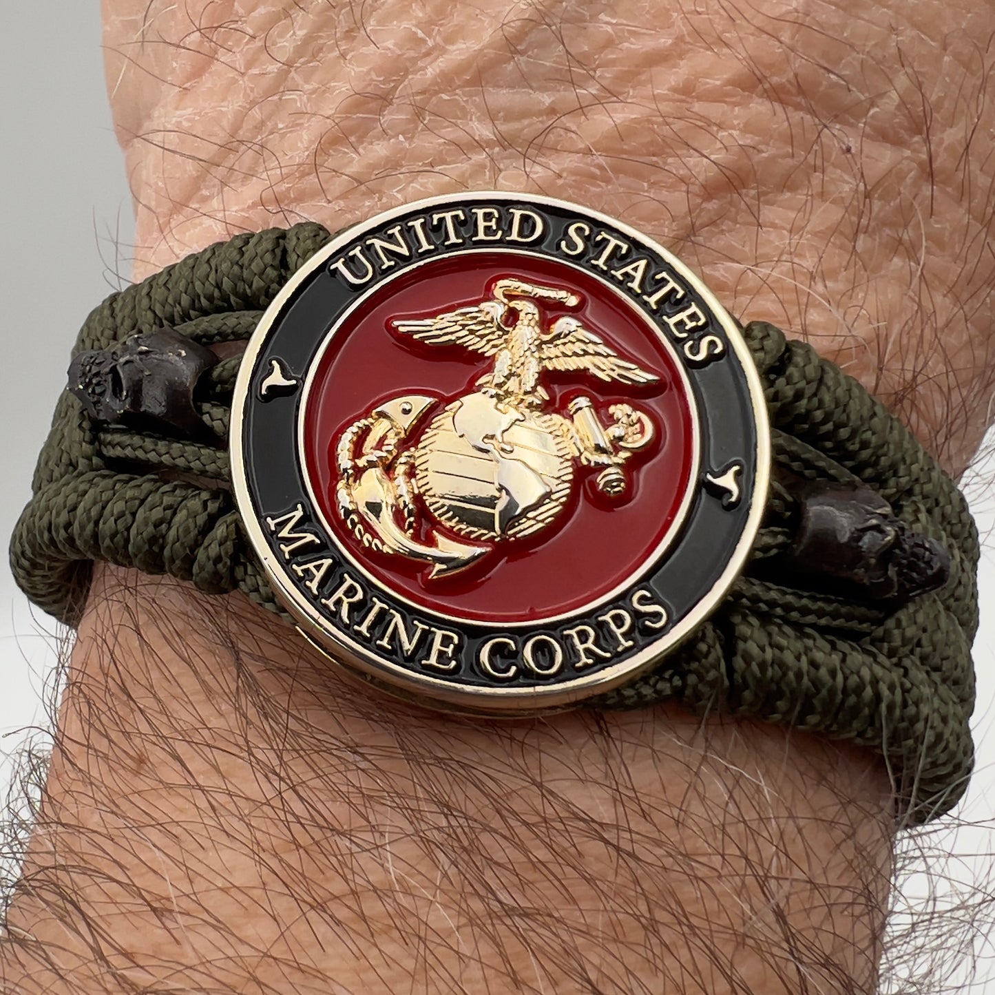 Thin, medium width, flexible and comfortable braided United States Marine Corps bracelet featuring a 24K gold plated USMC officer Eagle Globe and Anchor medallion, two black micro skulls, a black Cobra style tactical buckle and woven with Olive Drab Type-1 paracord.
